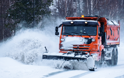An orange snowplow truck clearing snow from a road on a snowy day.