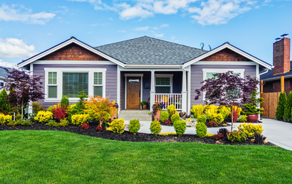 A purple bungalow with a well-kept lawn and colorful landscaping under a blue sky.