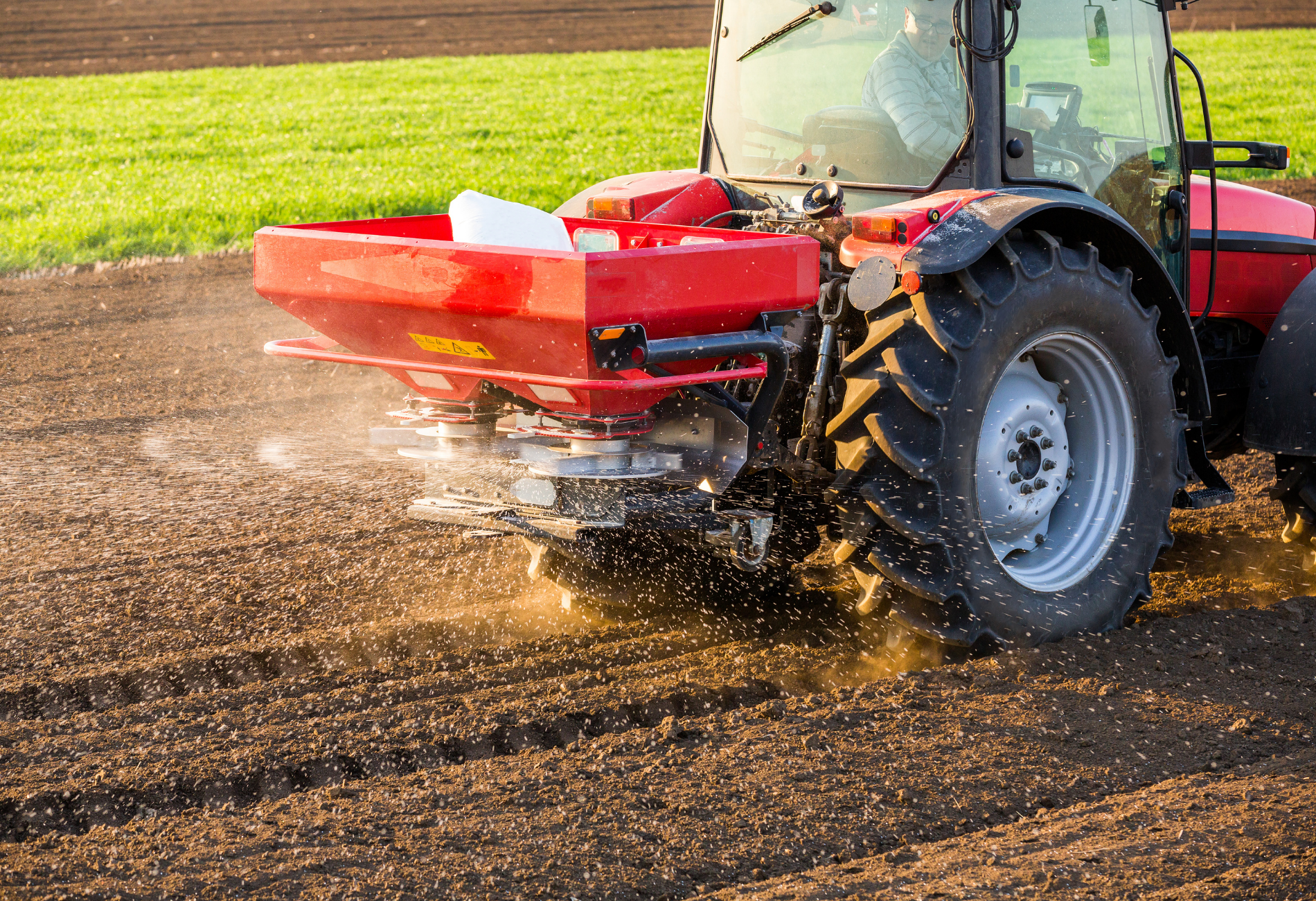 Red tractor spreading fertilizer in a field.