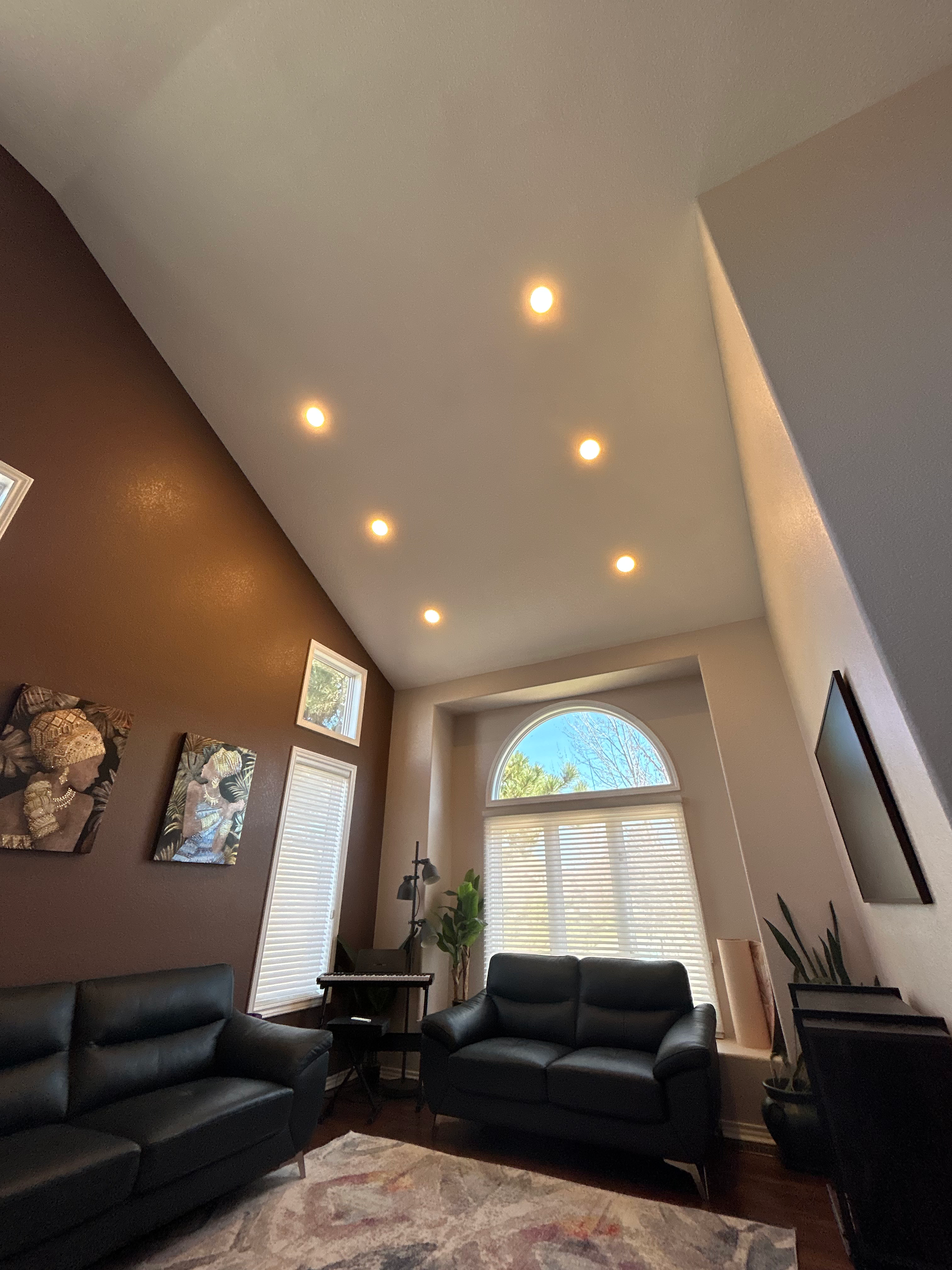 Living room with high ceilings, brown and beige walls, two black sofas, and arched window.