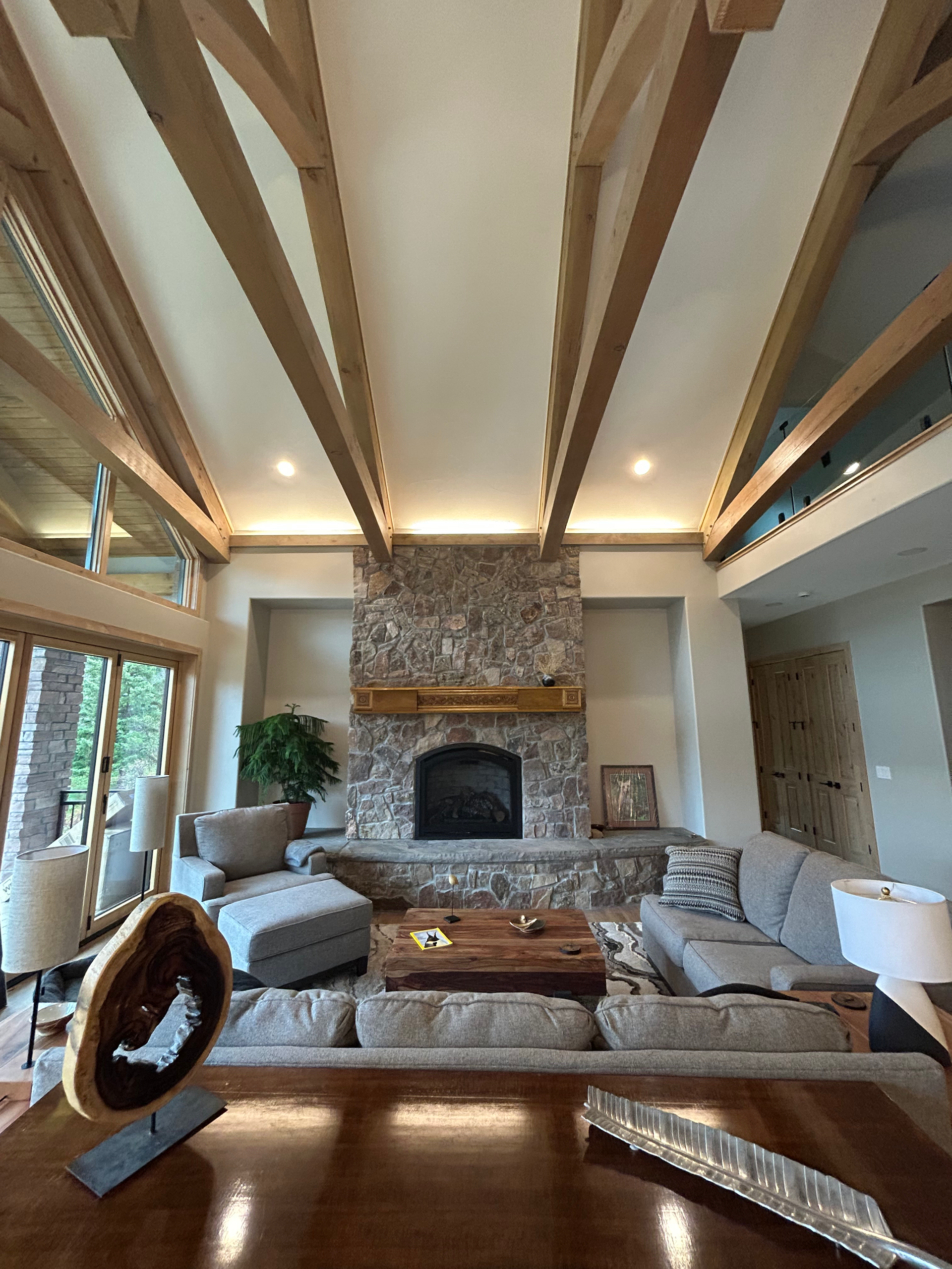 Living room with stone fireplace, exposed wooden beams, and neutral-toned furniture.