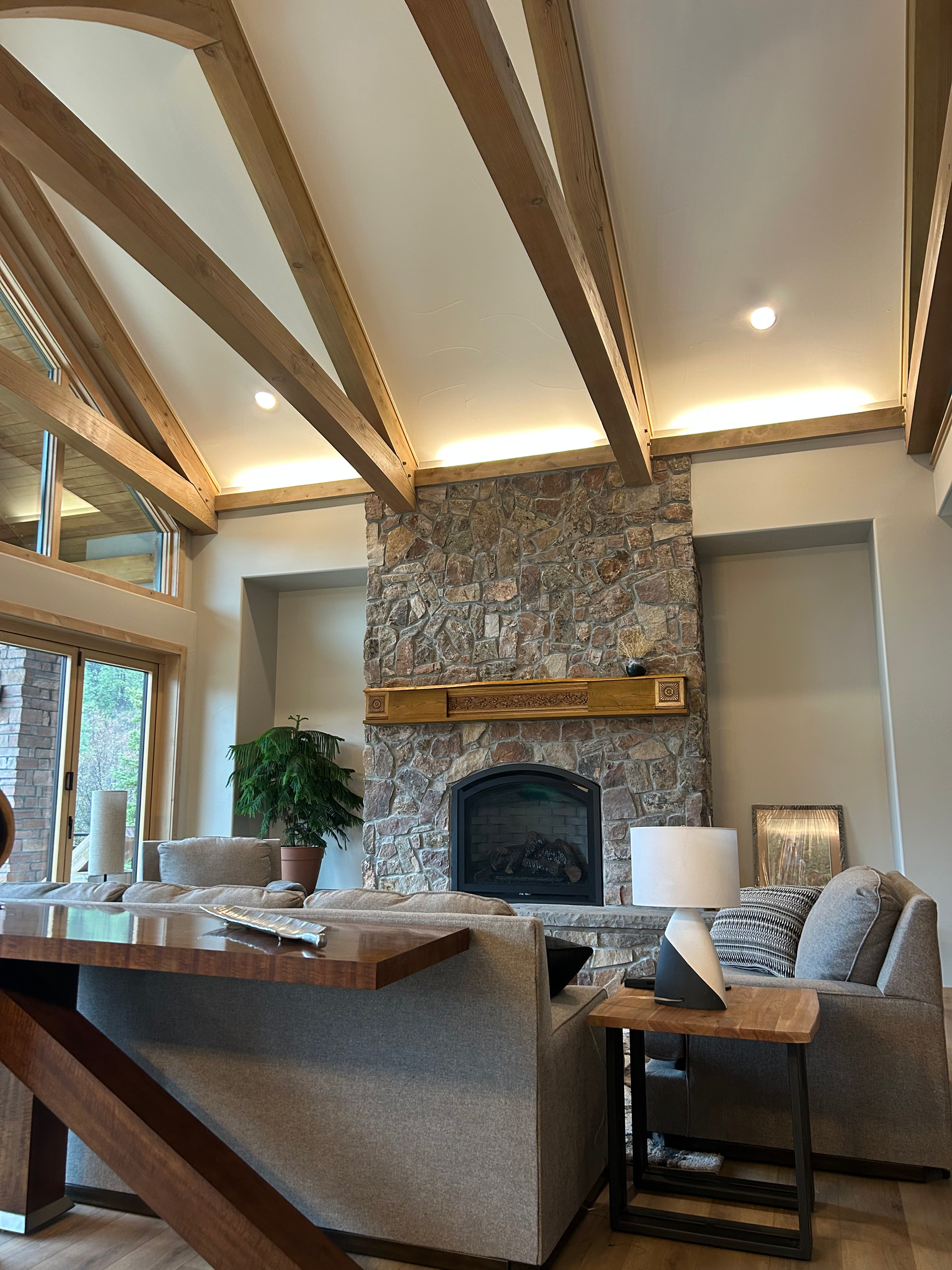 Living room with stone fireplace, vaulted ceiling, wood beams, and grey sofas.