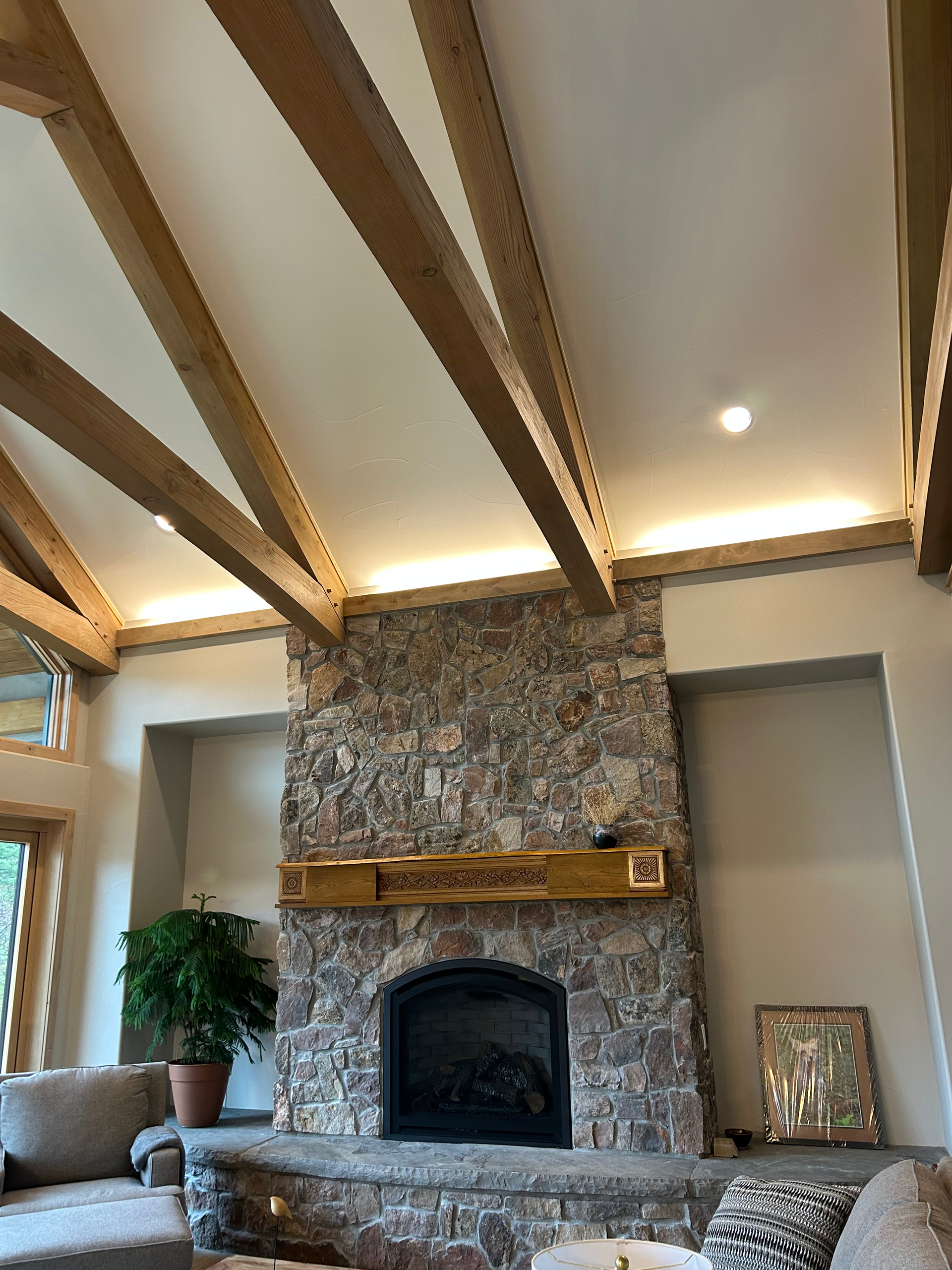 Fireplace with stone facade, wooden mantle, and vaulted ceiling with wood beams.