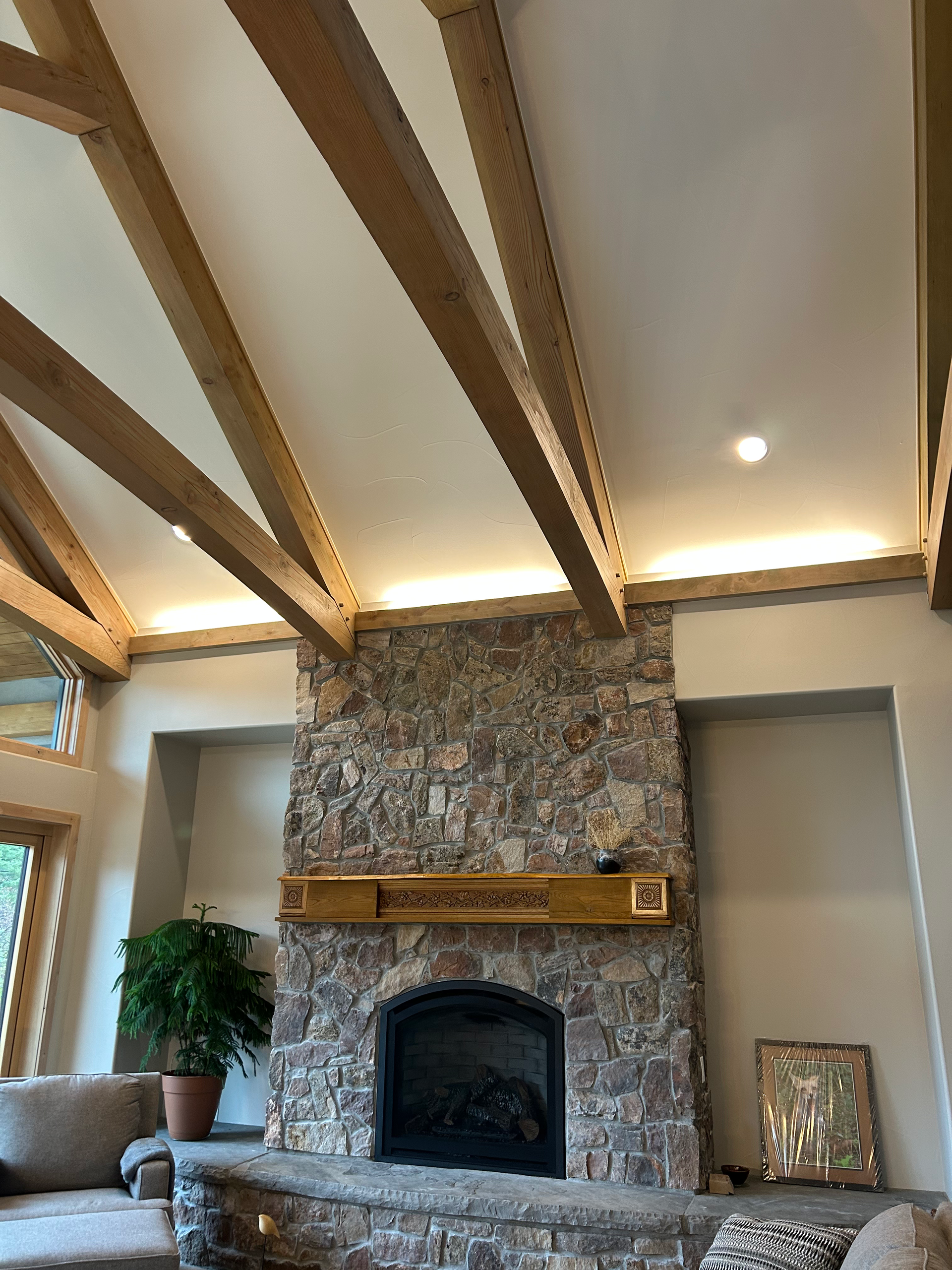 Stone fireplace with a wooden mantel, beneath a ceiling with wood beams and recessed lighting.