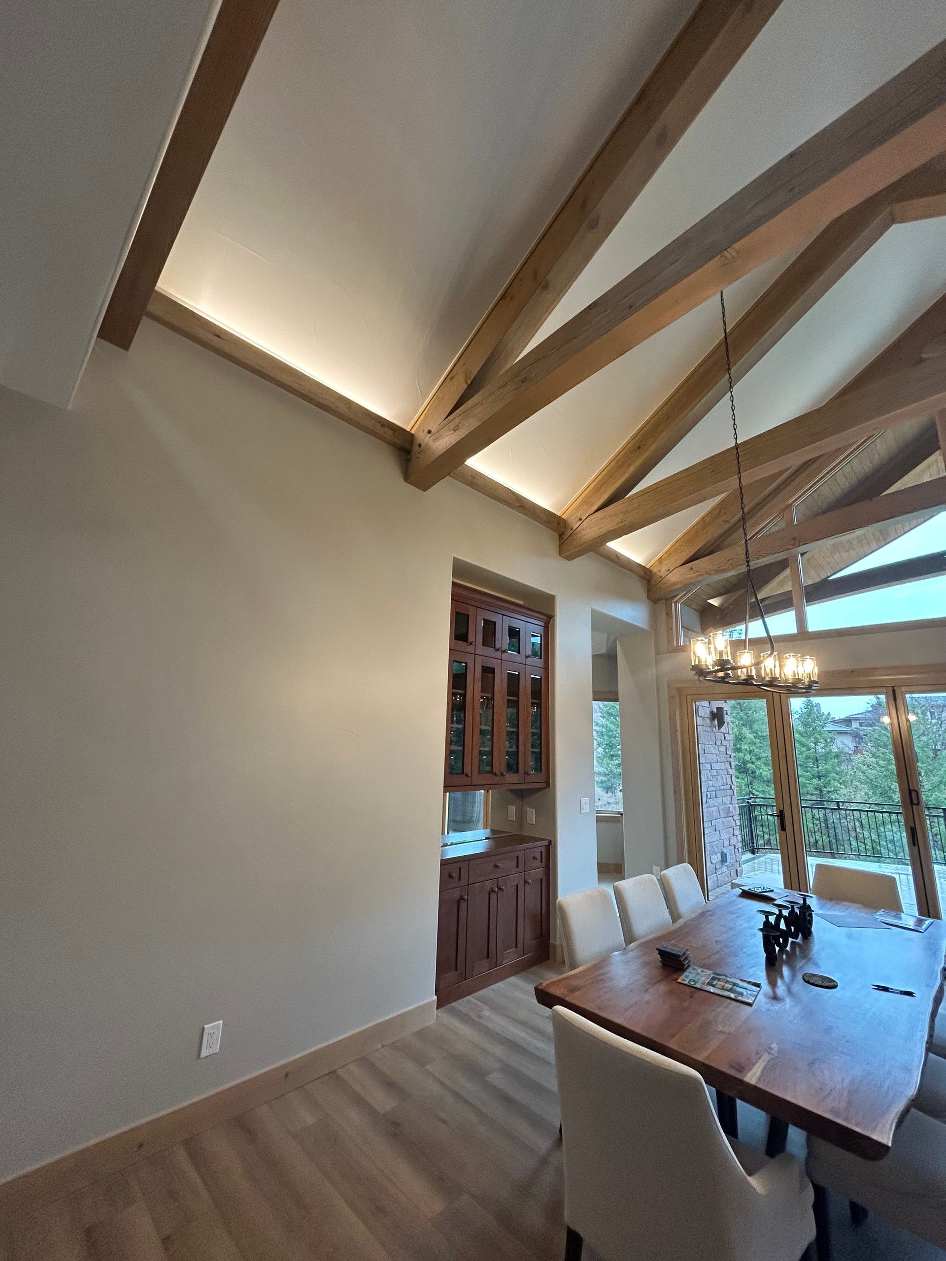 Dining room with wood beams, long table, chairs, and built-in cabinet. Neutral colors.