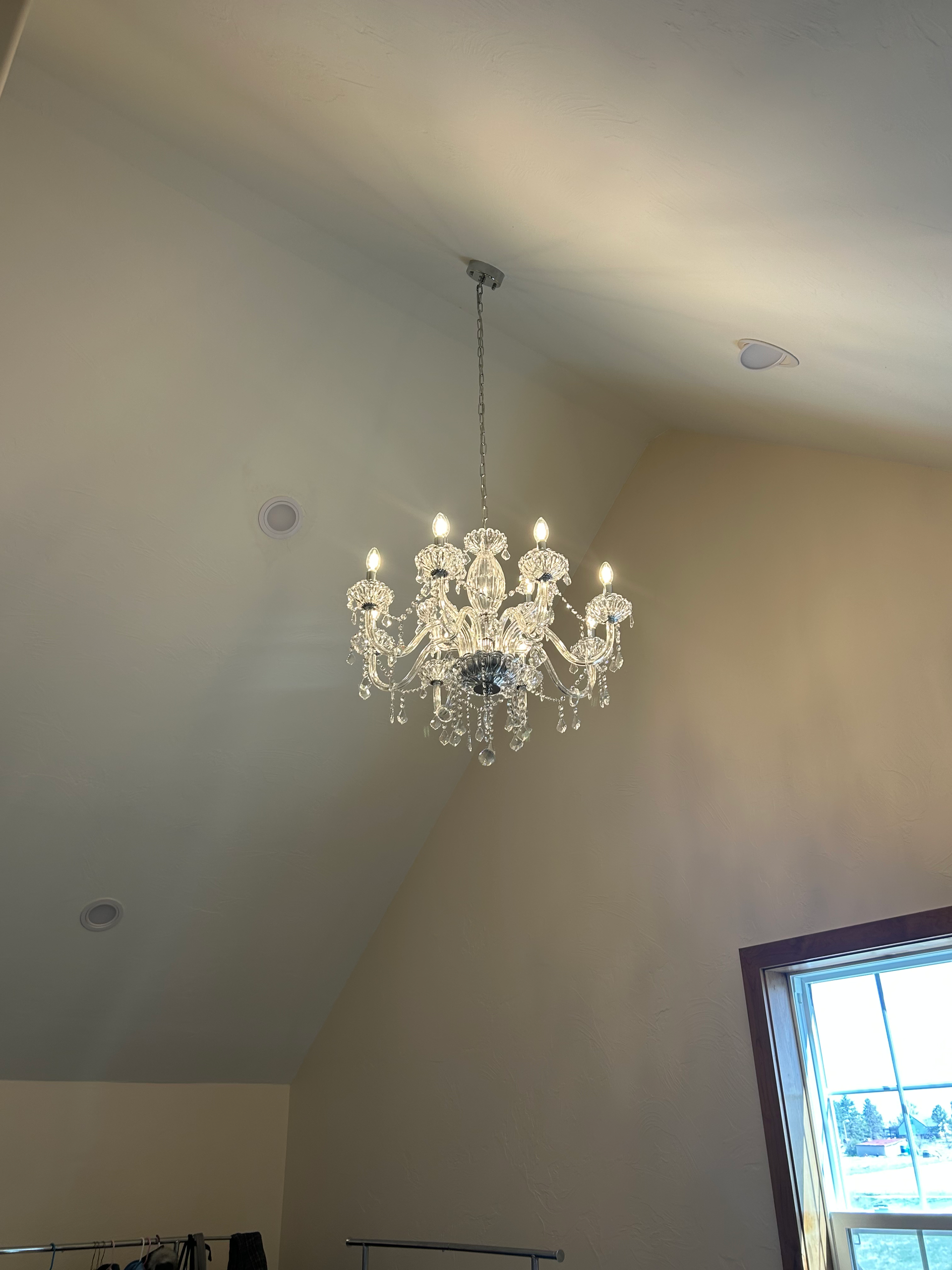 Chandelier hanging from a high ceiling with a window on the right. The walls are a pale color.