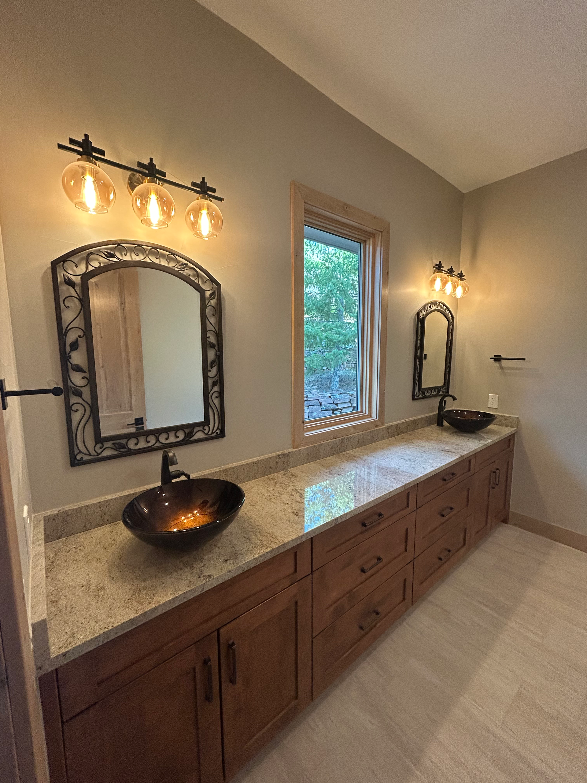 Bathroom with two sinks, wooden cabinets, and decorative mirrors. Soft lighting and neutral colors.