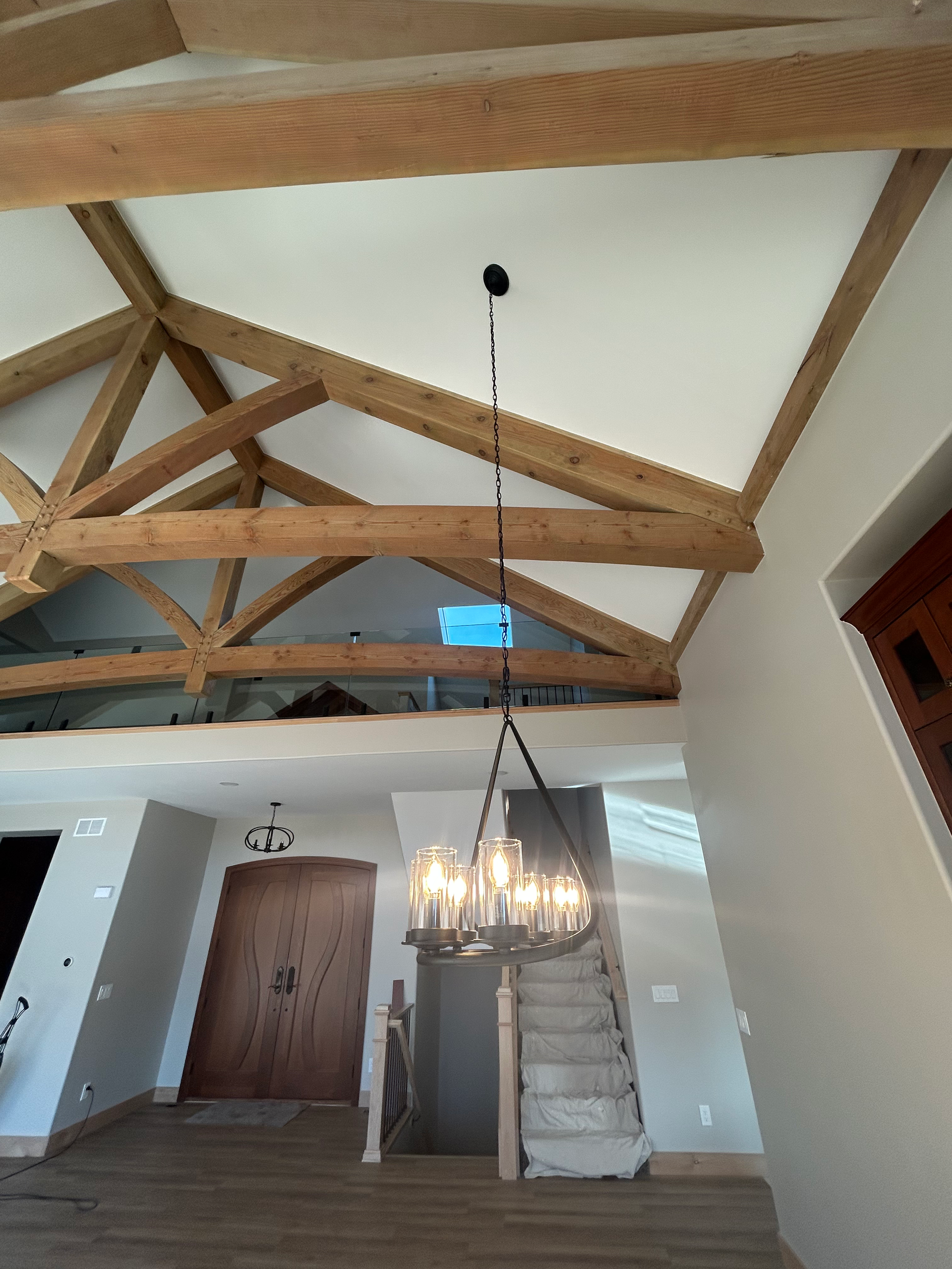 Vaulted living room with wooden beams, chandelier, stairs, and front door.