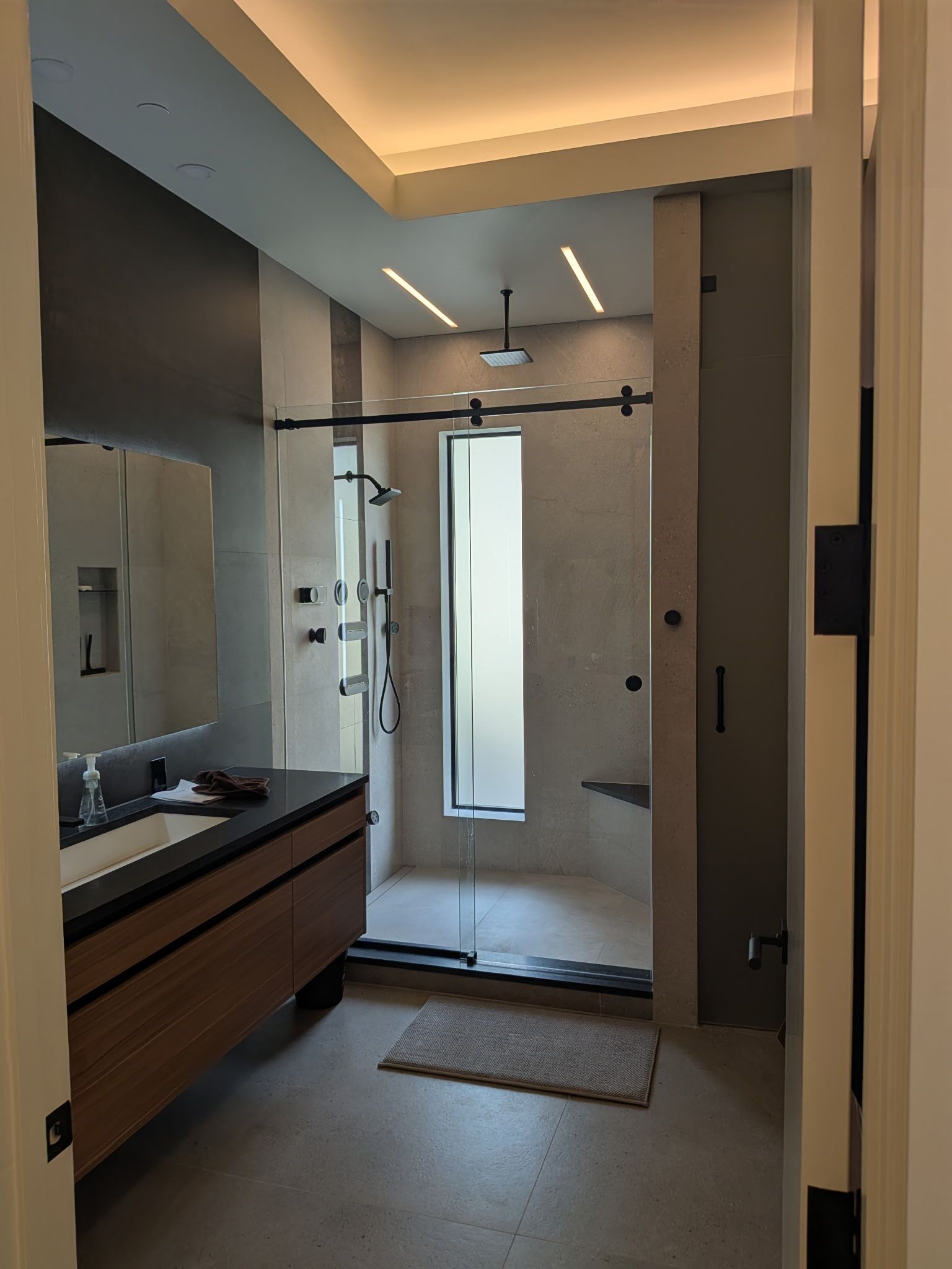 Modern bathroom with glass shower, dark vanity, and gray walls.
