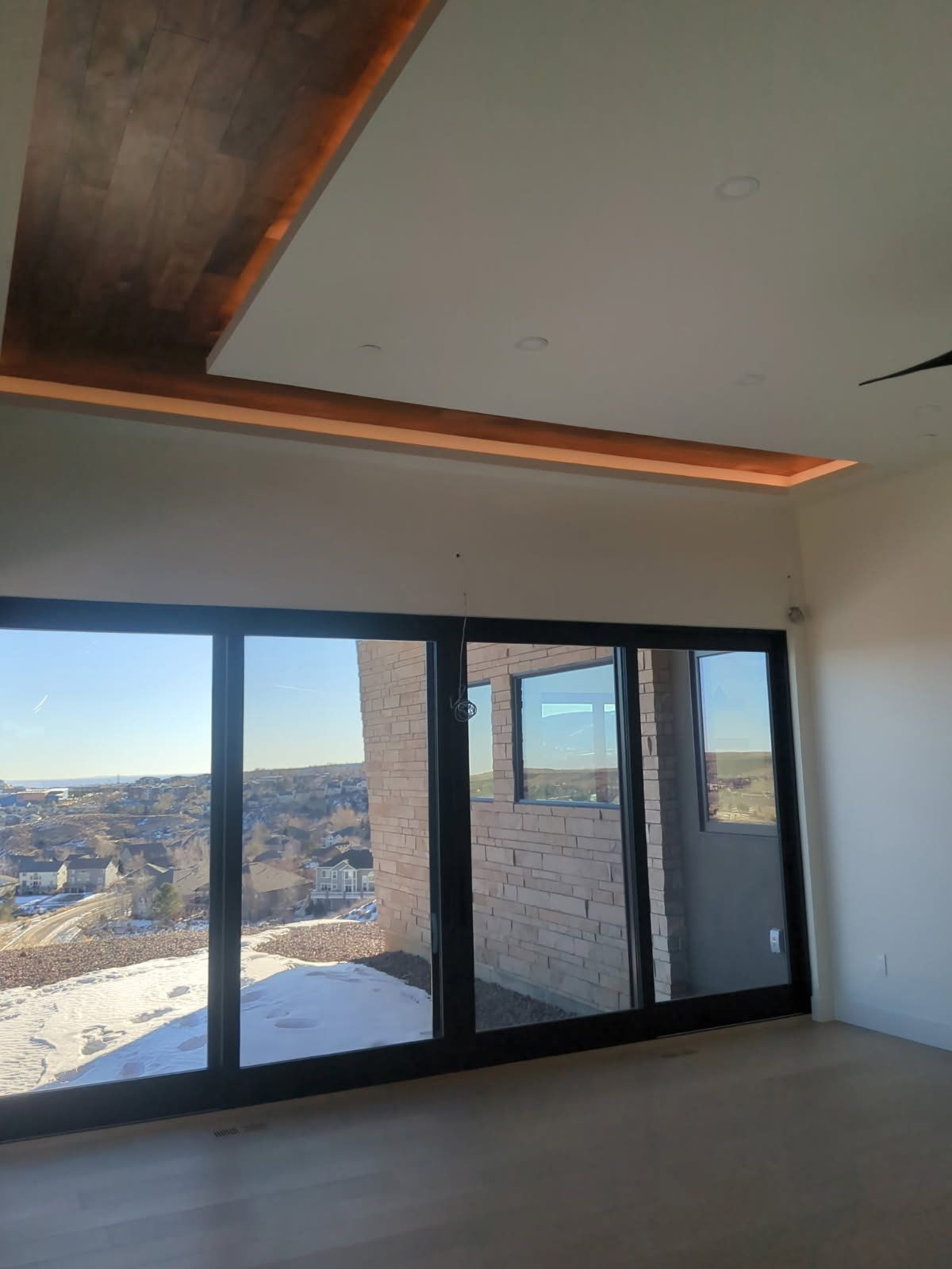 Modern room with large windows, light-colored floor, ceiling wood detail, and city view.