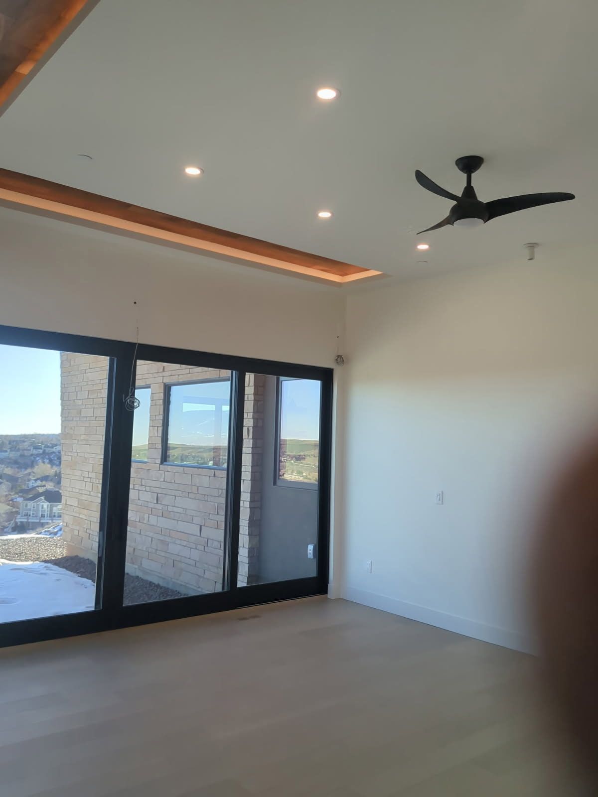 A modern room with large sliding glass doors, recessed lighting, a black ceiling fan, and light wood floors.