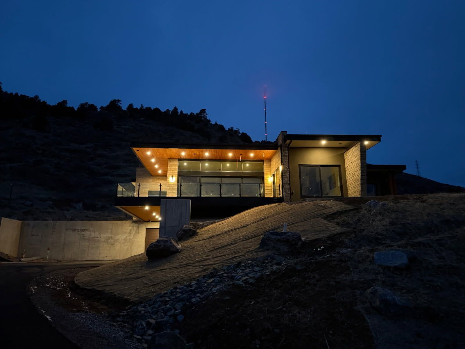Modern house lit up at dusk on a hillside, with a dark blue sky.