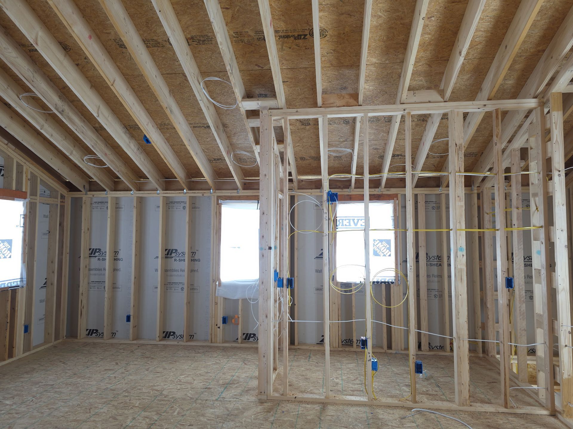 Interior view of a room under construction. Wooden framing of walls and ceiling, windows, and wiring.