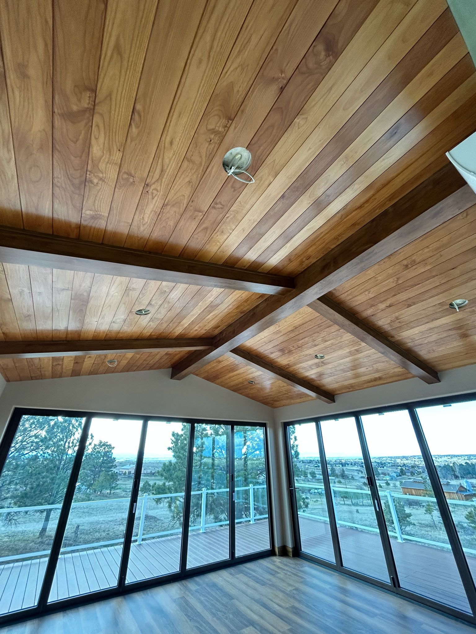 Wooden ceiling with beams, surrounded by large windows overlooking an outdoor scene.