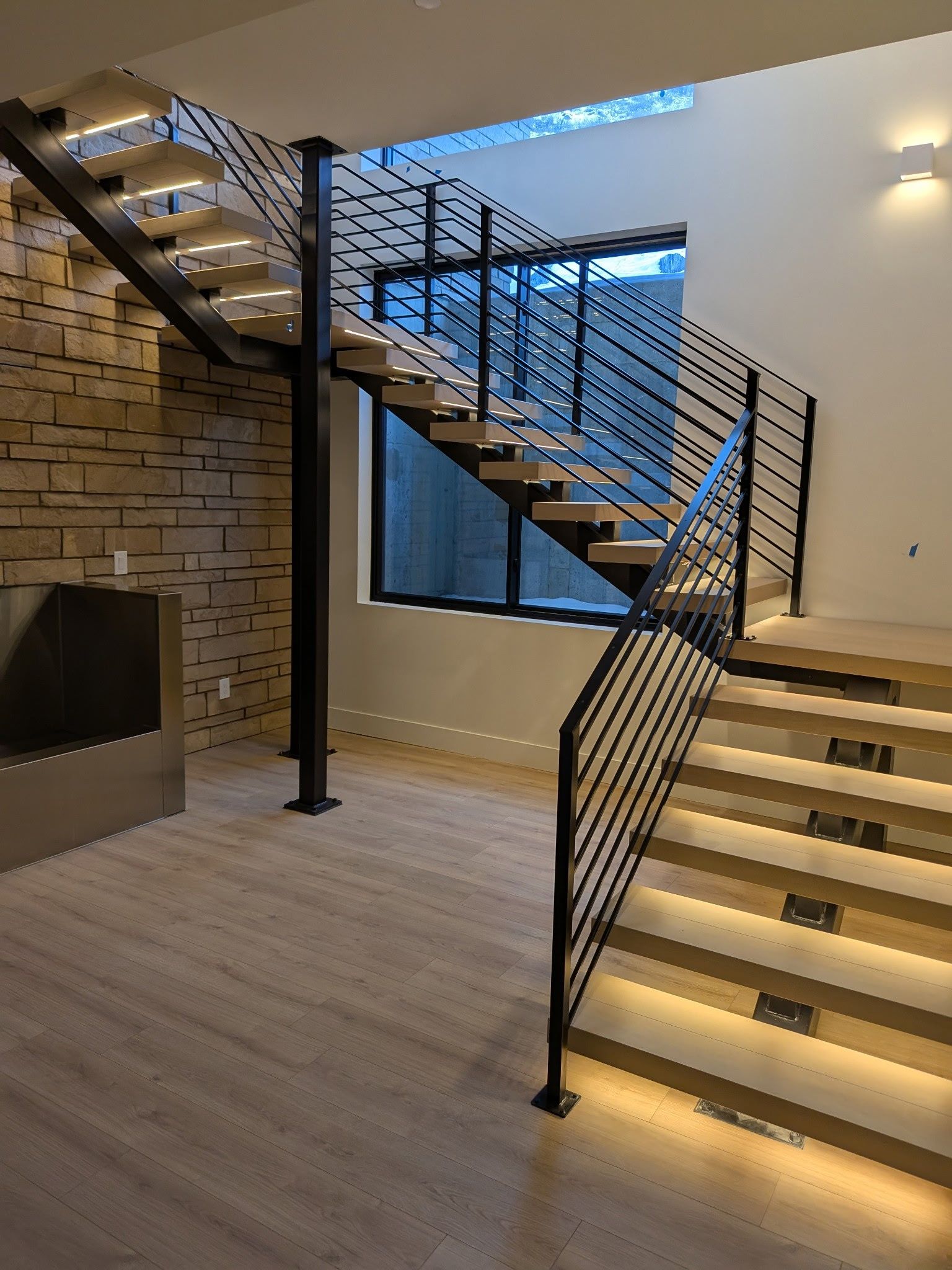 Modern staircase with metal railings, wooden steps, and under-step lighting.