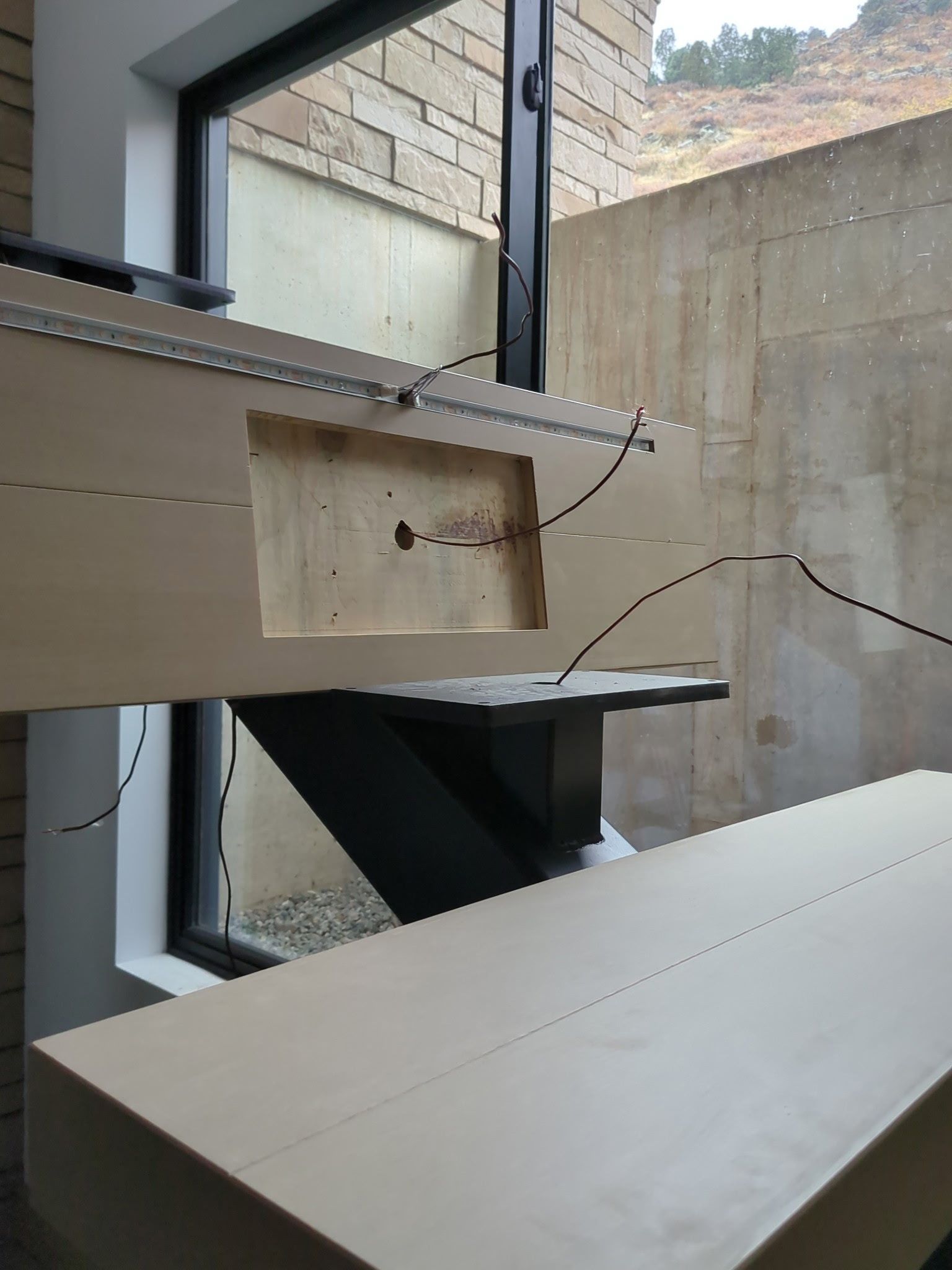 Close-up of a modern light-colored wood desk with a dark metal support structure.  Window and stone wall in the background.
