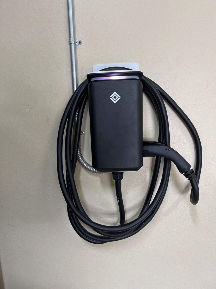 A black electric car charger is hanging on a wall.