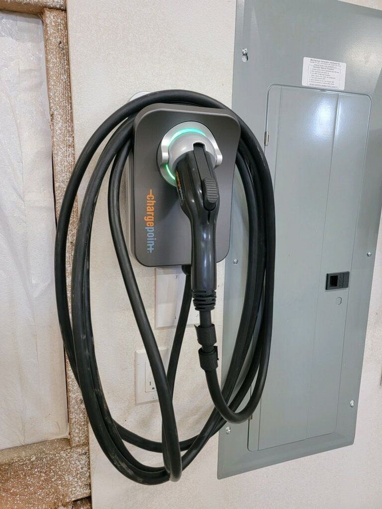 A charger is hanging on a wall next to a breaker box.