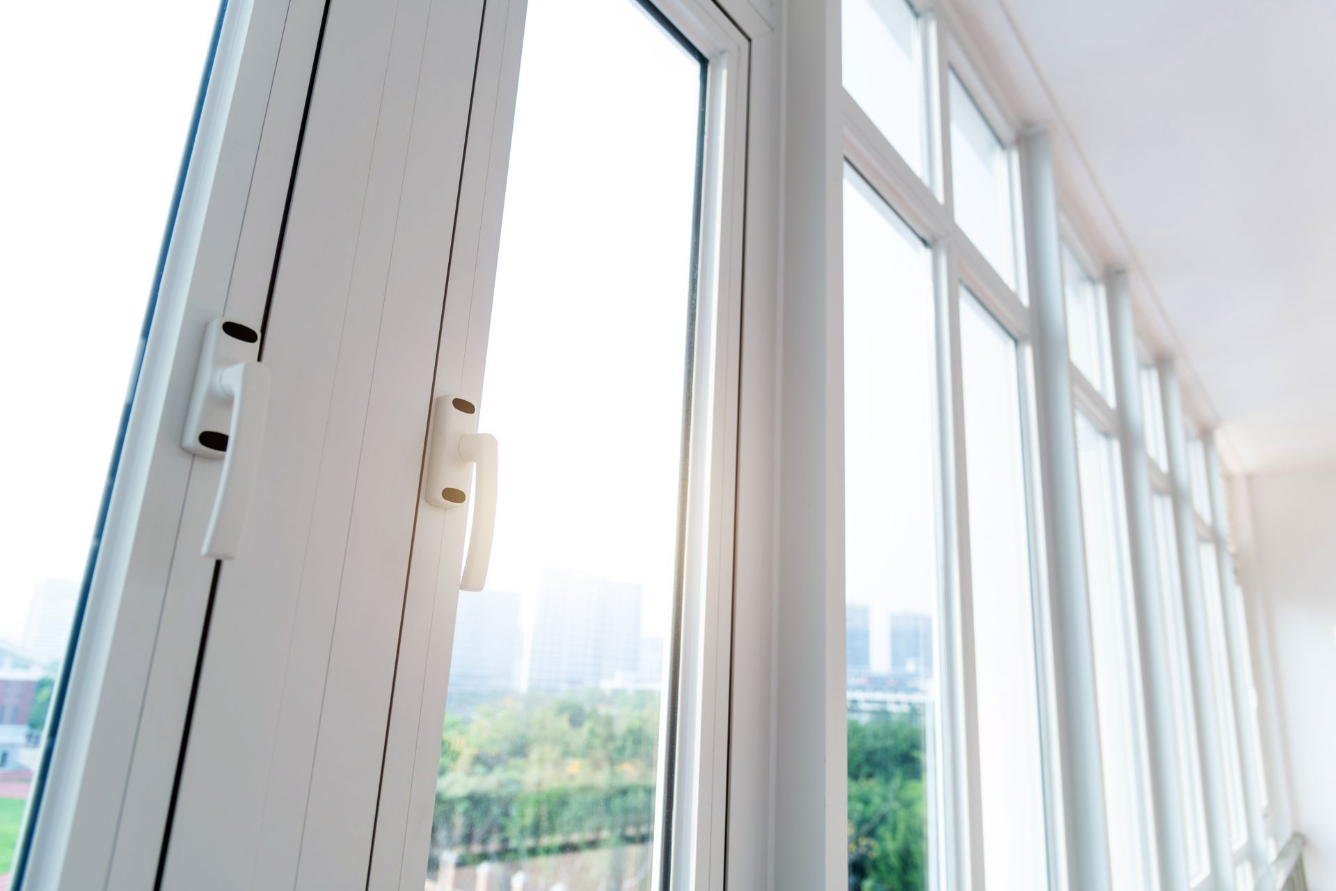 Open white window with a view of a city through the glass, bright natural light.