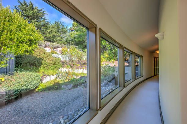 Curved hallway with large windows overlooking a lush garden. Daylight streams in, illuminating the interior.
