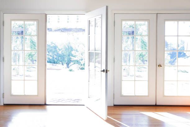 White French doors open to a bright outdoor space with sunlight streaming in, illuminating a wood floor.