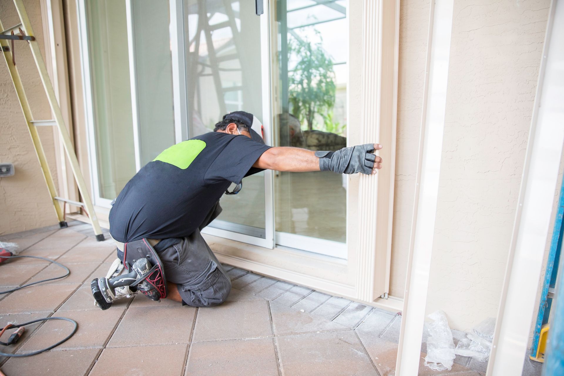 Person installing a sliding glass door. They're on their knees, wearing gloves, working on the frame.