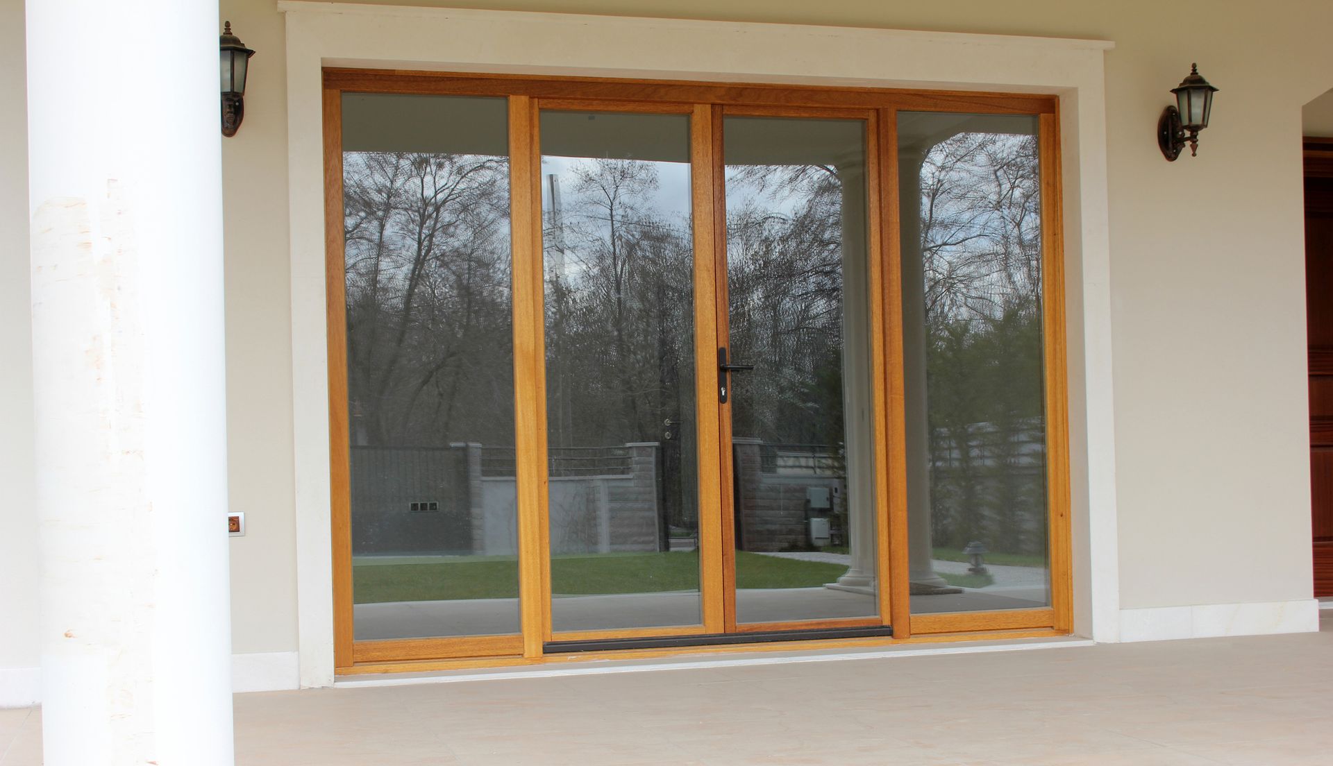 Sliding glass doors with wooden frames. Trees reflected in the glass. Beige building exterior.