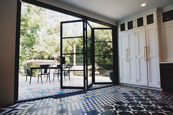 Open black-framed glass doors to patio; patterned tile floor, white cabinets with gold handles.