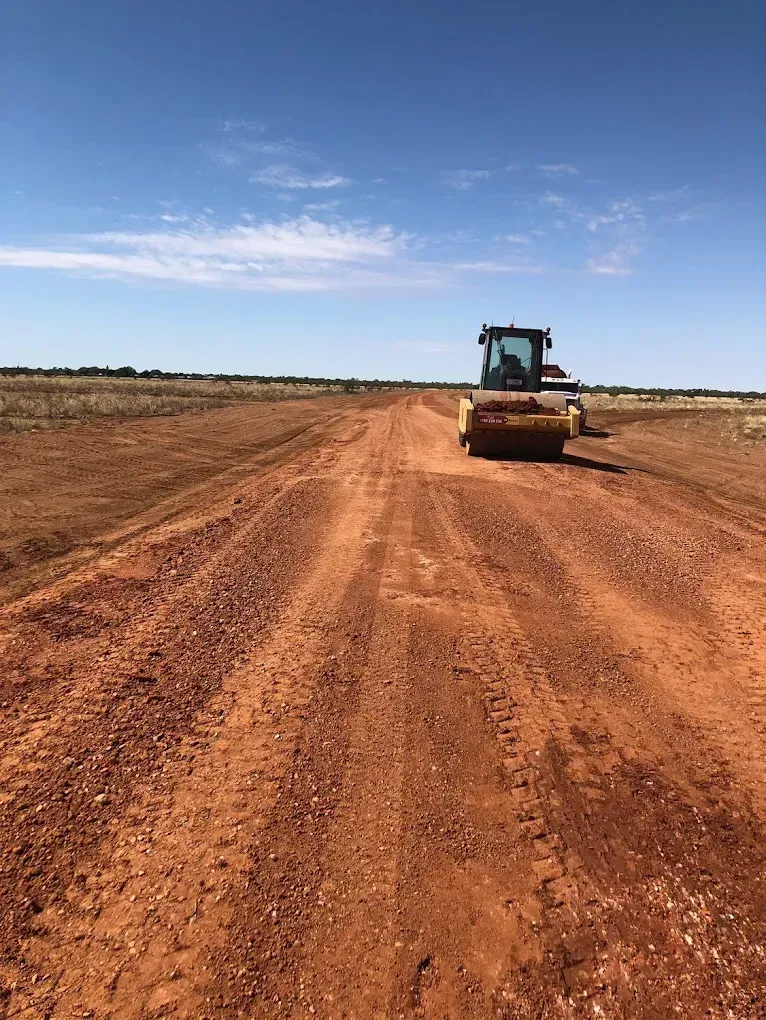 A road roller compacting a red dirt road under a clear blue sky — Lamont Civil Services Pty Ltd In Townview, QLD