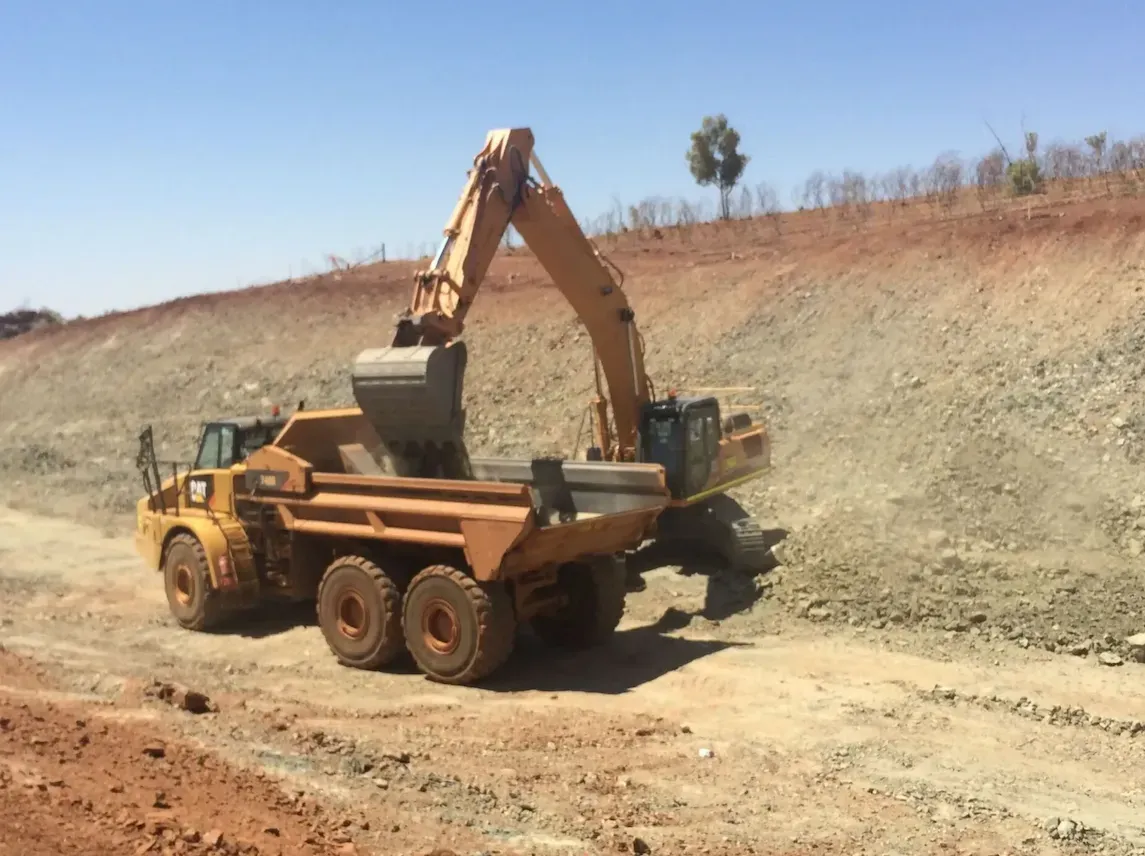 An Excavator Loading Dirt Into A Dump Truck On A Dirt Road — Lamont Civil Services Pty Ltd In Townview, QLD