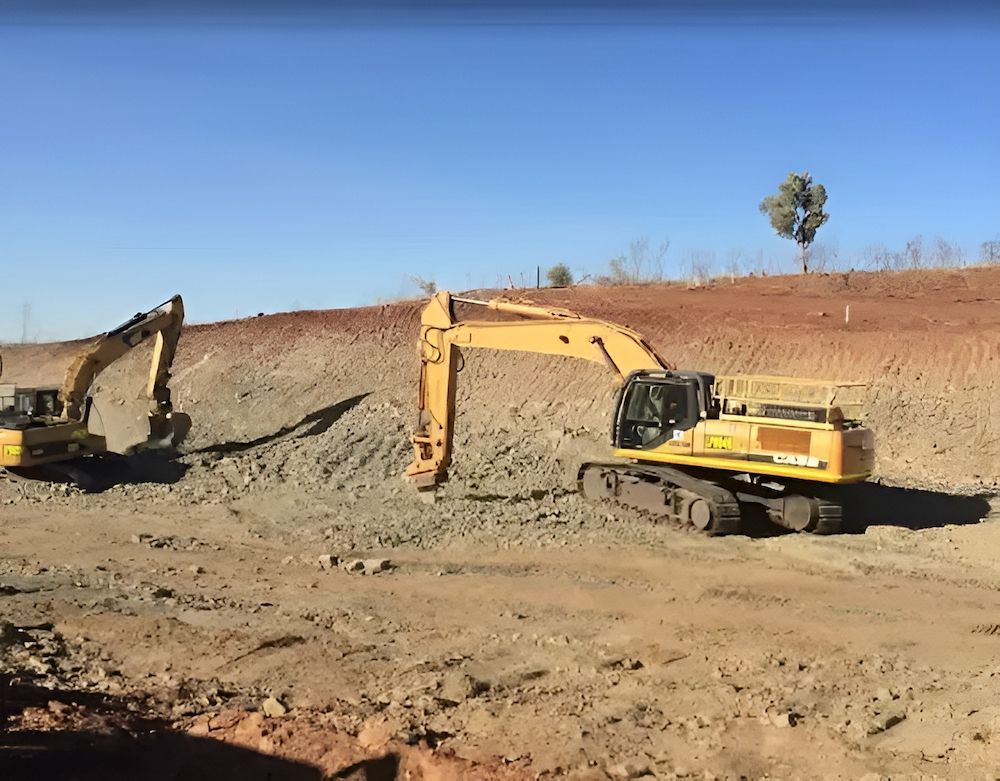 Two Yellow Excavators on a Dirt Construction Site Under a Clear Blue Sky — Lamont Civil Services Pty Ltd In Mount Isa, QLD
