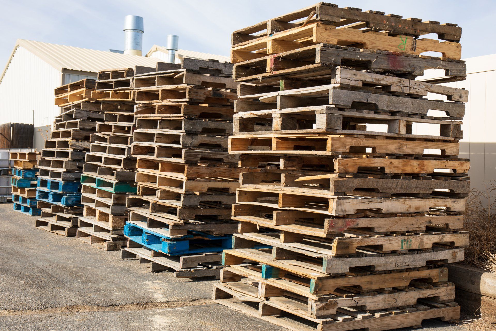 Wooden pallets stacked along a wall in a warehouse lot.