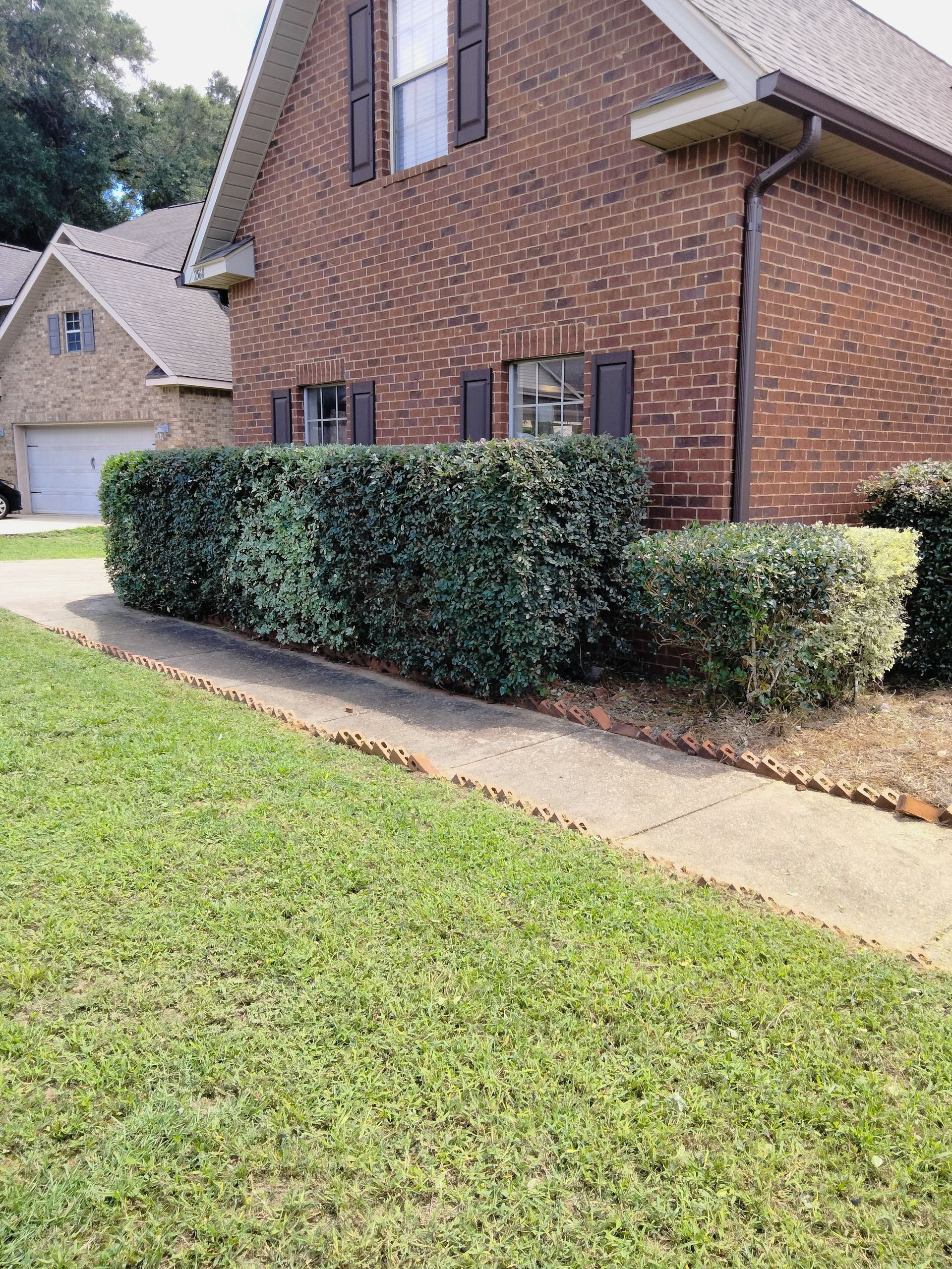 A brick house with a lush green lawn and a sidewalk in front of it.