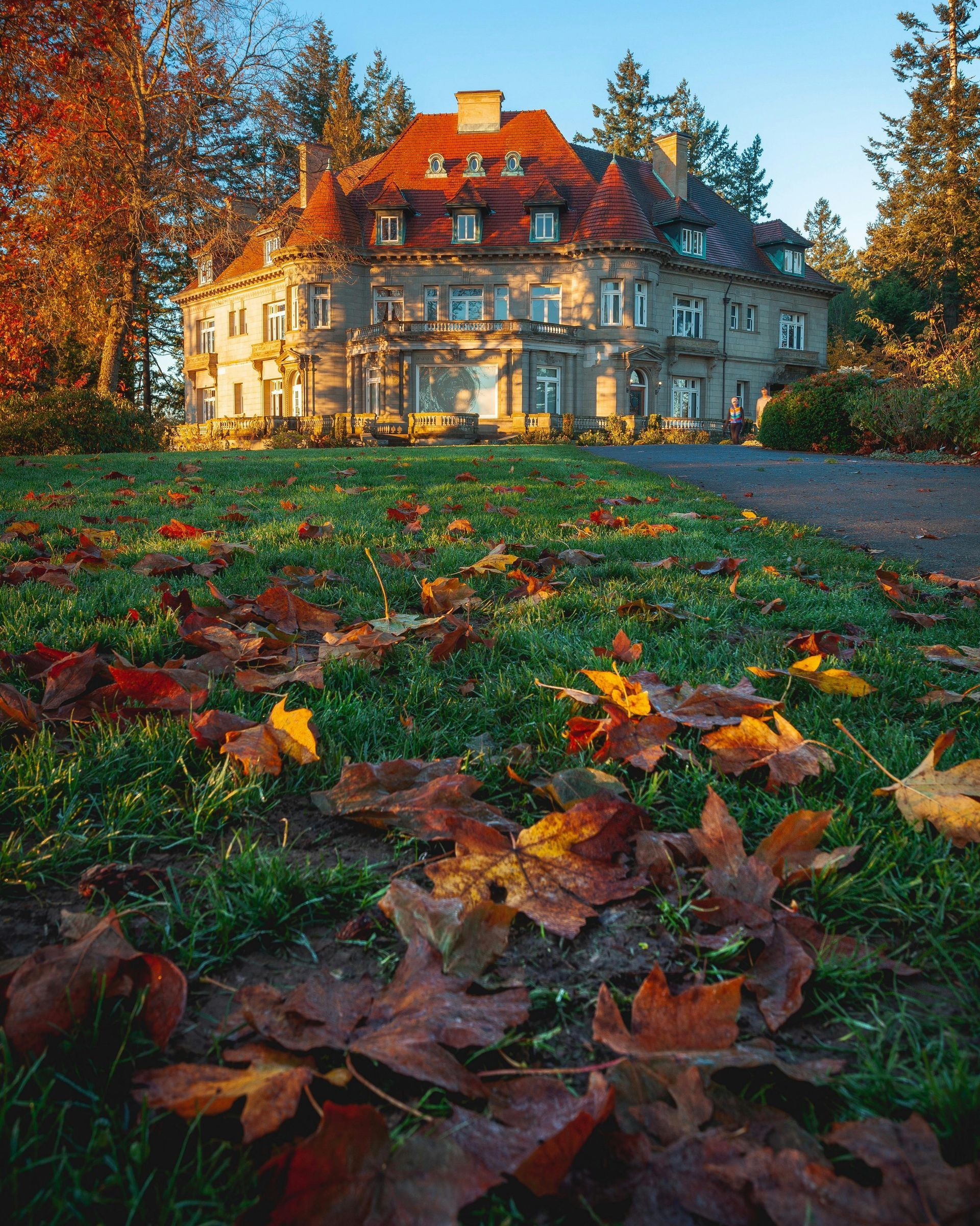 Grand, multi-story mansion on a hill, surrounded by trees with autumn leaves, and a sunny sky.