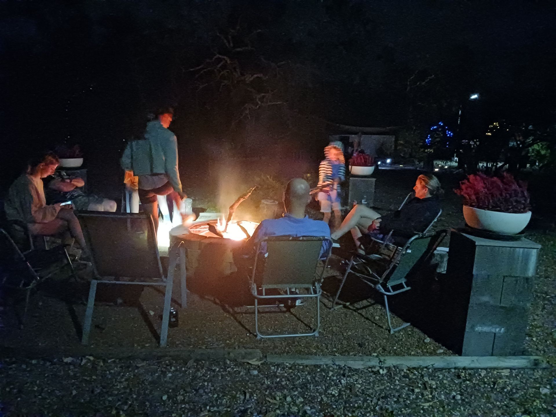 A group of people are sitting around a fire pit at night.