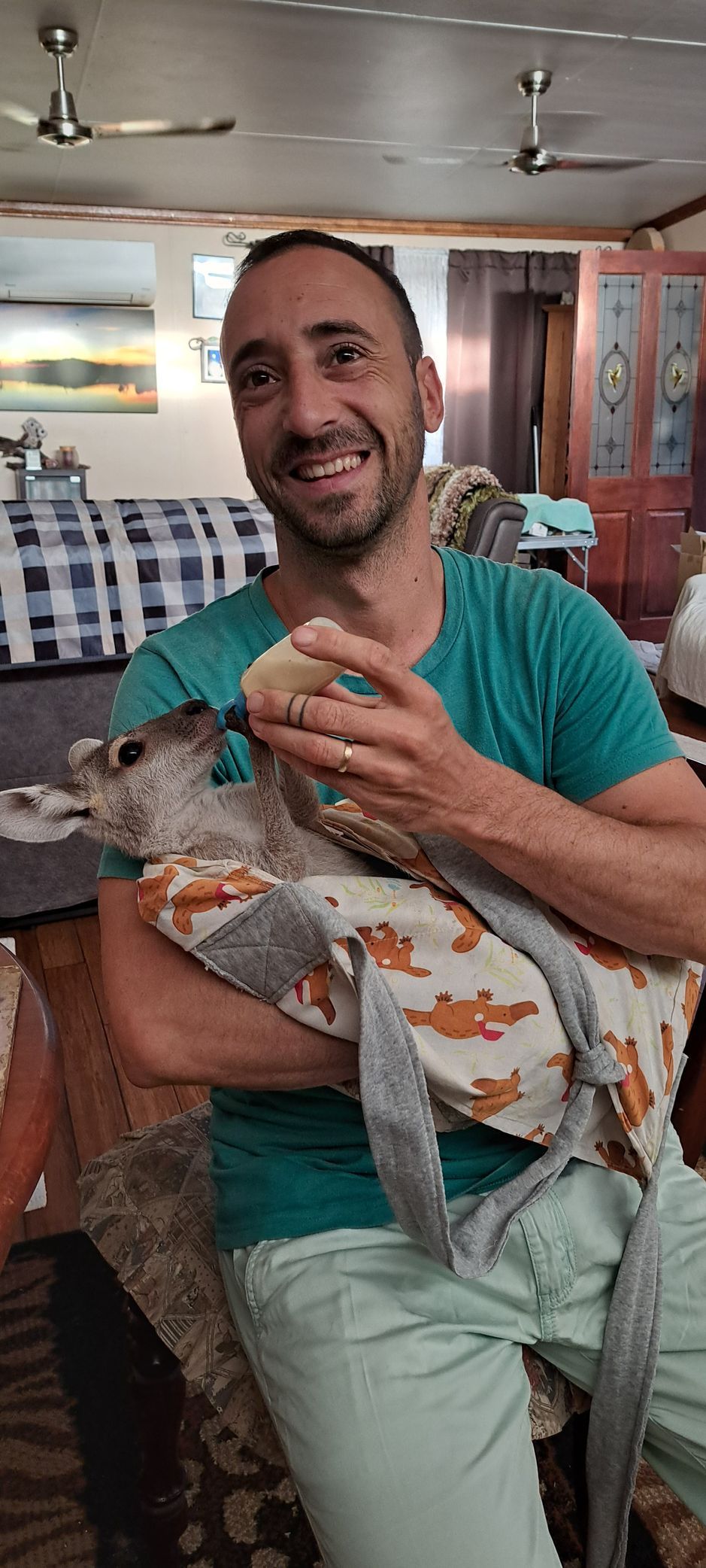 A man is holding a kangaroo in his arms in a living room.