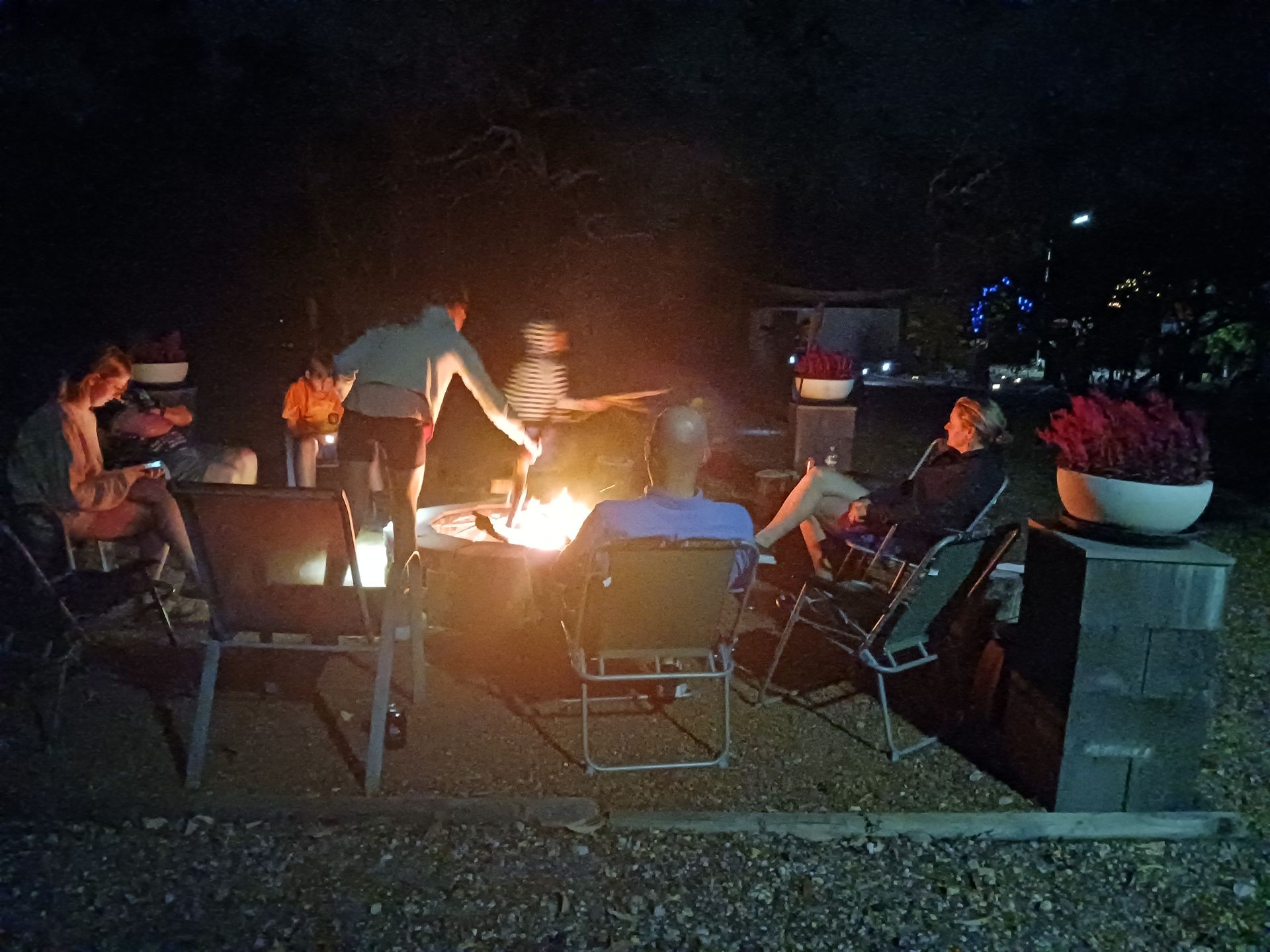 A group of people are sitting around a fire pit at night.
