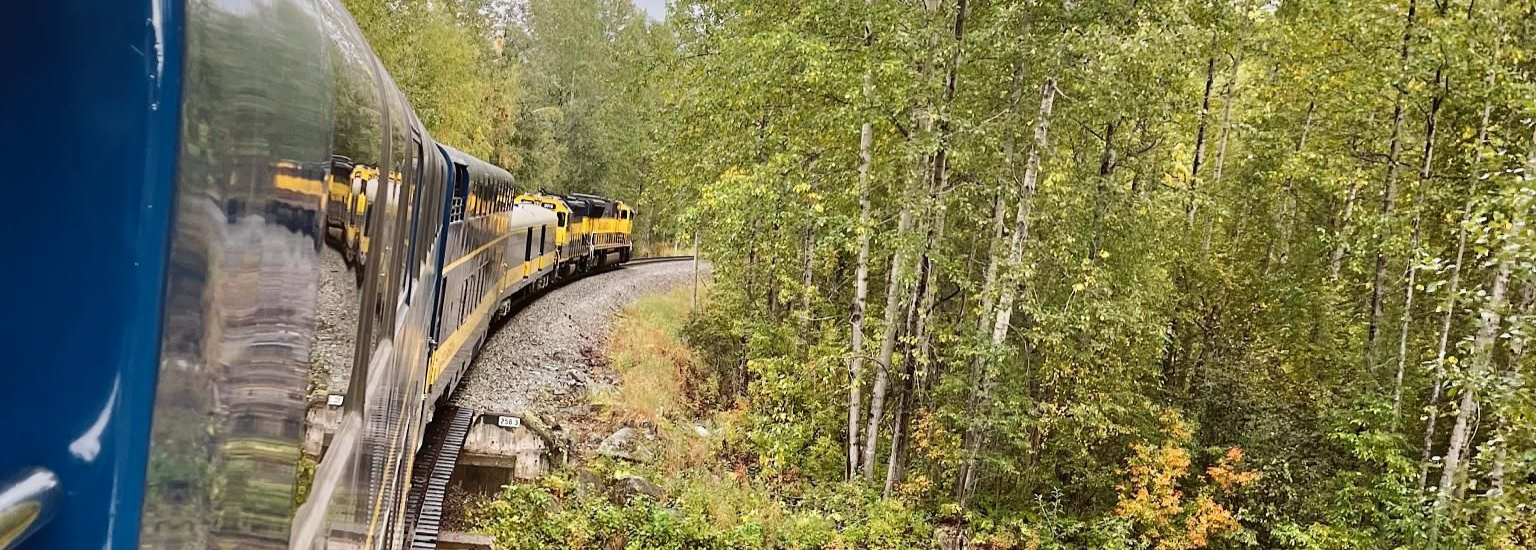 Spacious modern living room with dining area, beige and gray tones, large windows, and a colorful rug.