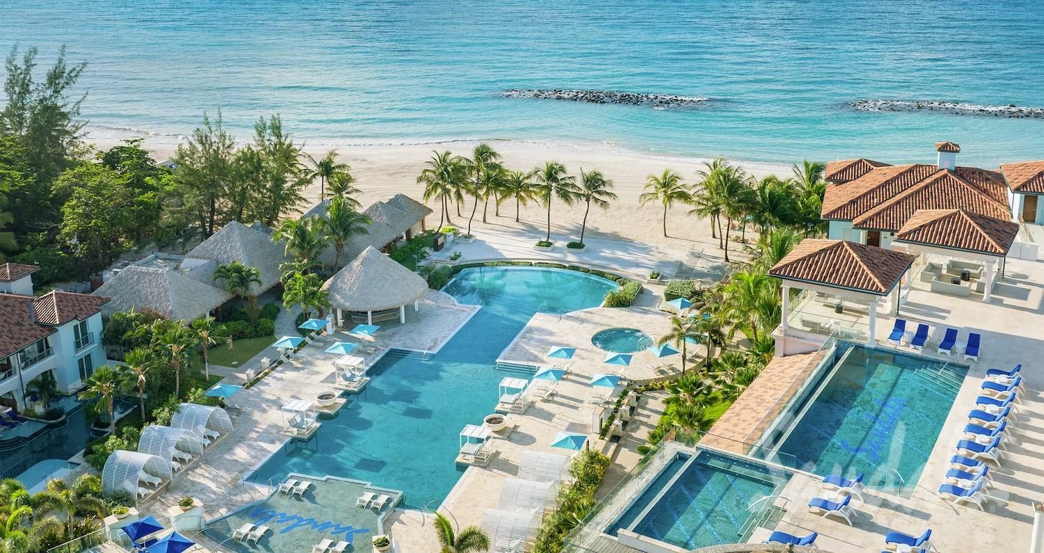 Aerial view of a resort with pools, beach, palm trees, and ocean in the Bahamas.