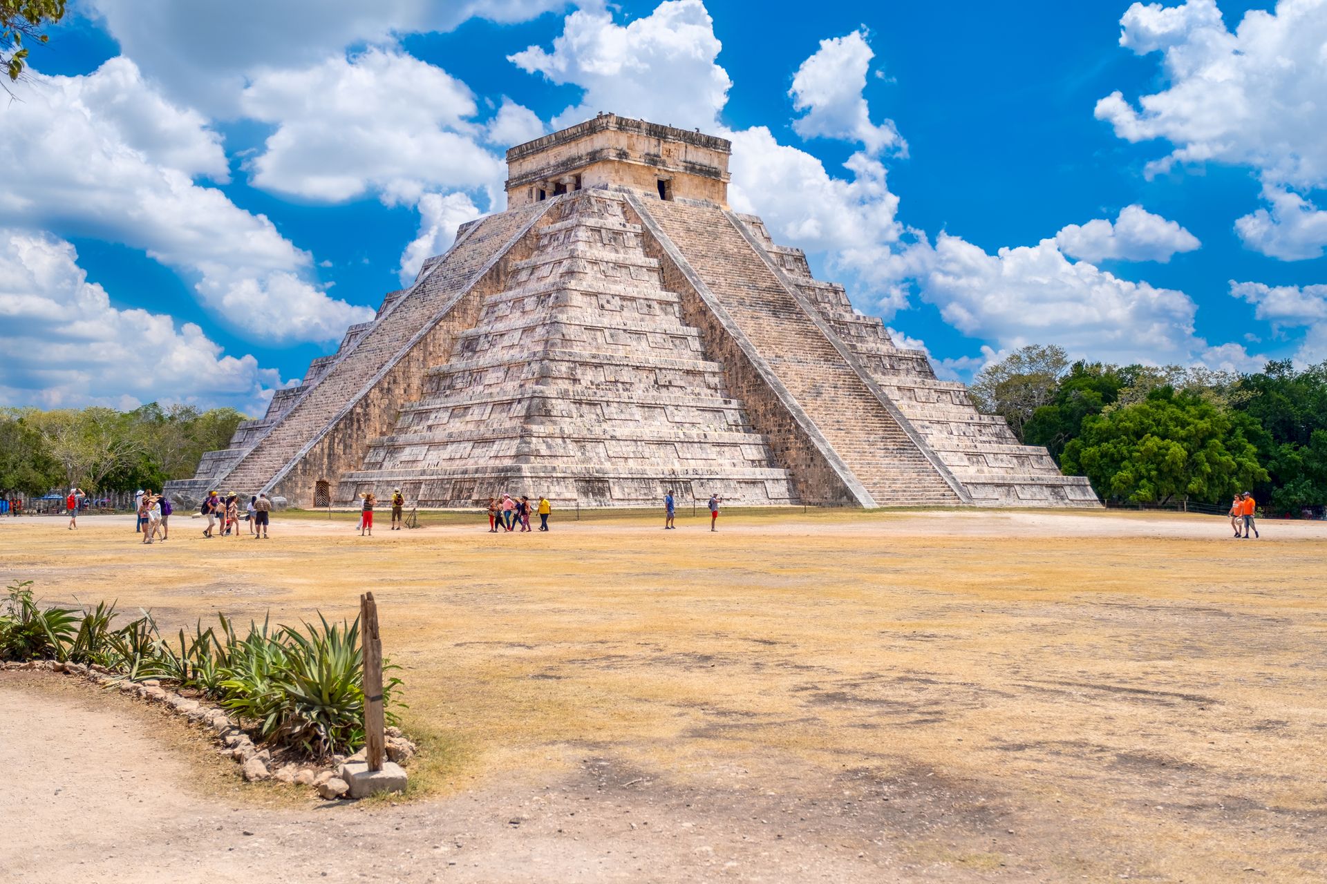 Chichen Itza pyramid, ancient Mayan structure in Mexico, with blue sky and people in the foreground.