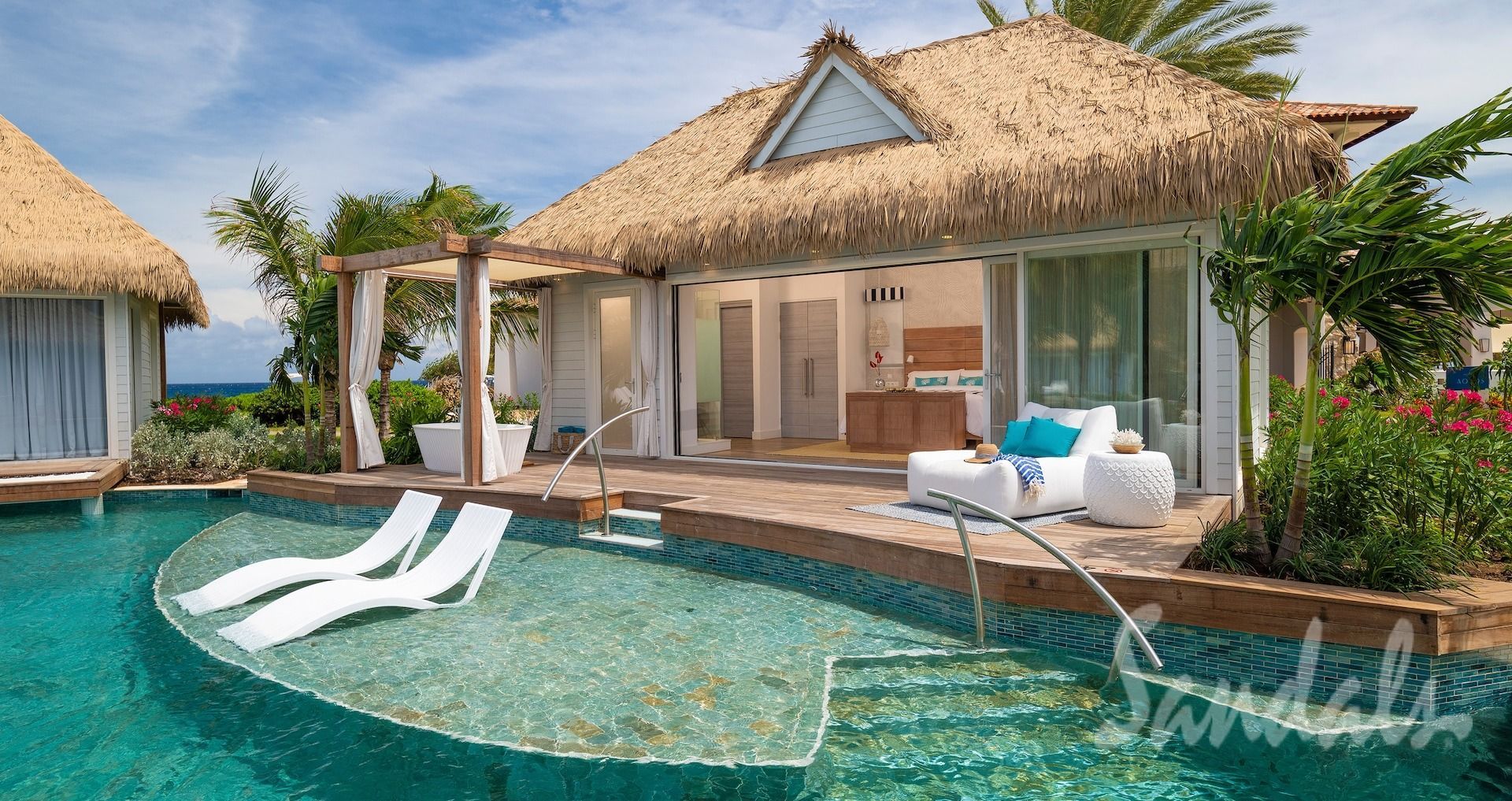 Tropical overwater bungalow with pool, blue water, white lounge chairs, and a thatched roof.