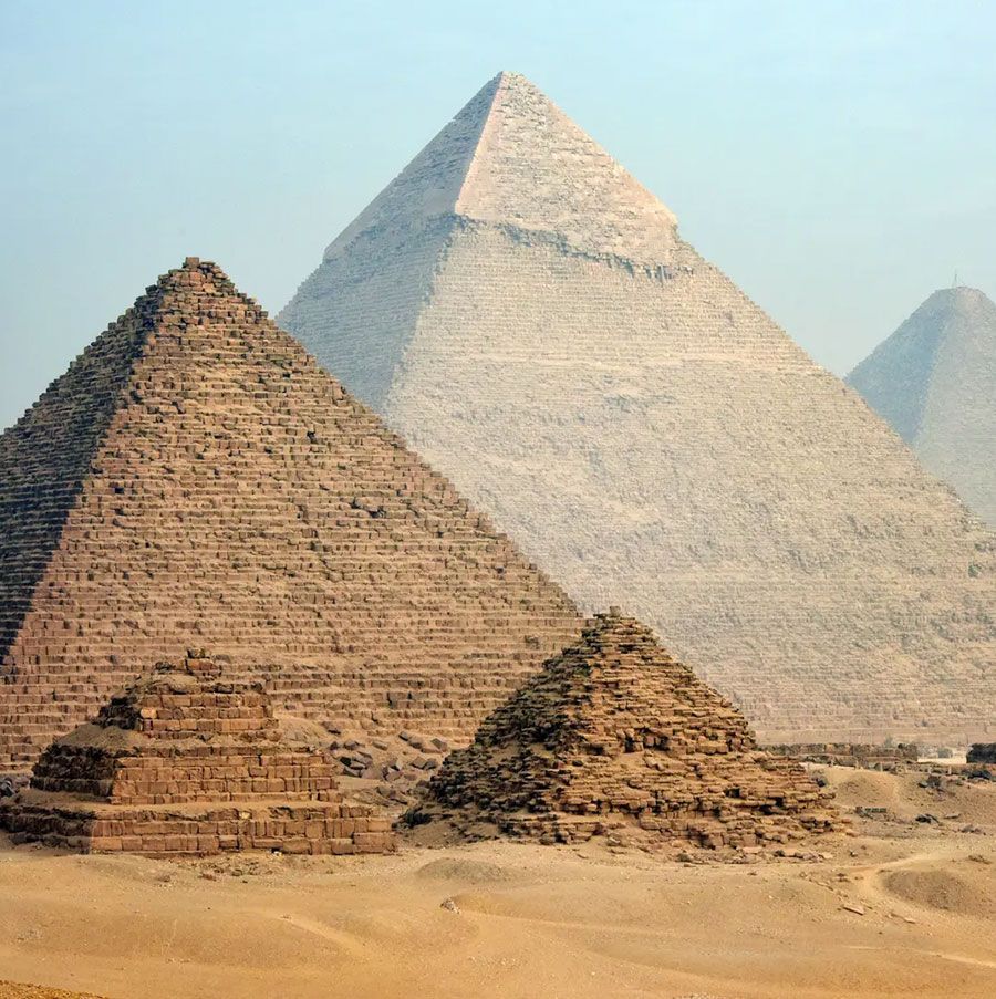 Pyramids of Giza in Egypt, ancient structures of brown stone in a desert landscape under a hazy sky.