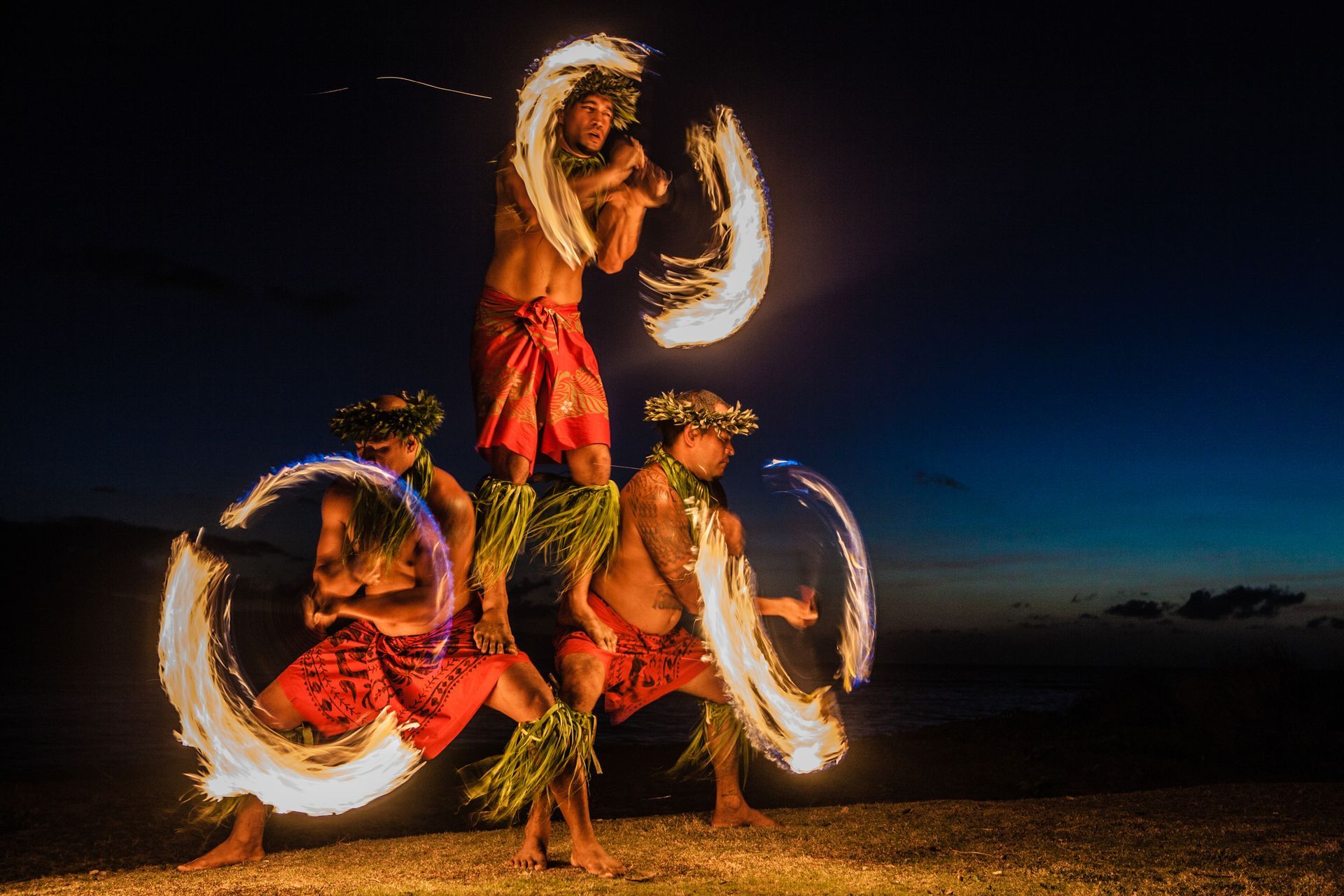 Fire dancers perform with flaming hoops on a beach at dusk.
