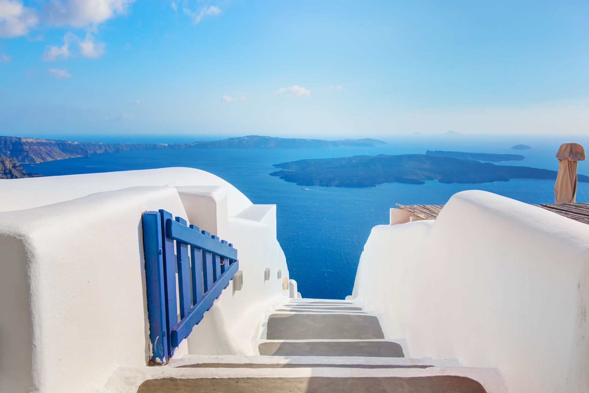 White buildings with blue gate and stairs overlook the Aegean Sea in Santorini, Greece.