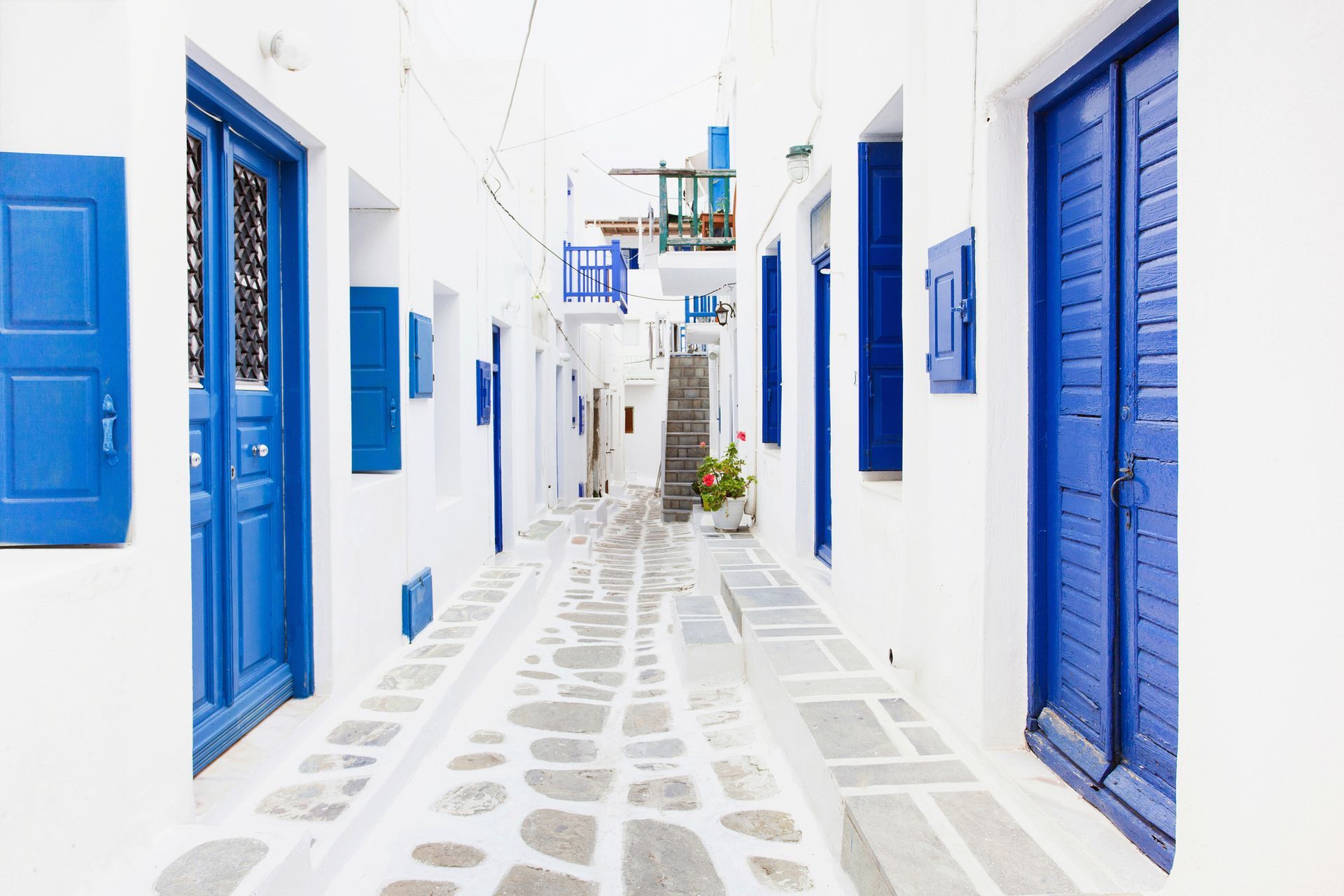 Whitewashed alleyway in Greece with blue doors and shutters, cobblestone pathway.