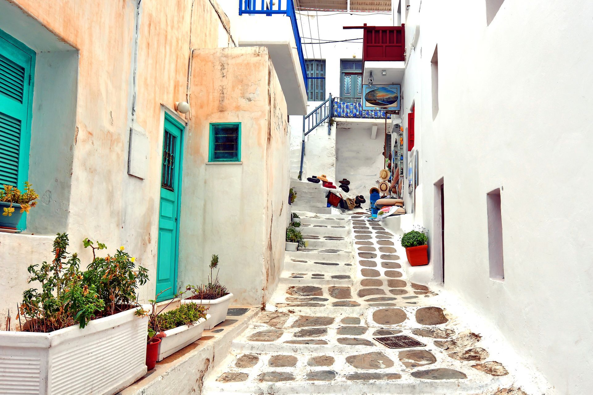 Narrow cobblestone street in a Greek village, white buildings with teal and red accents.