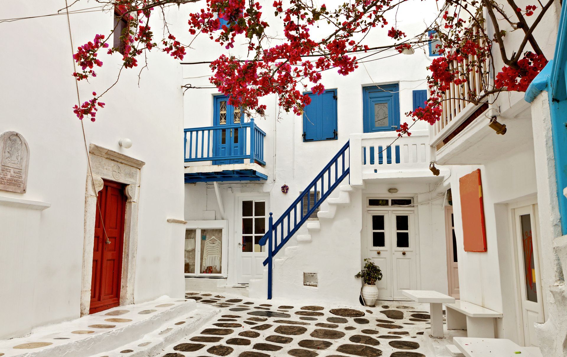 White buildings with blue accents, red door and flowers, cobblestone street.