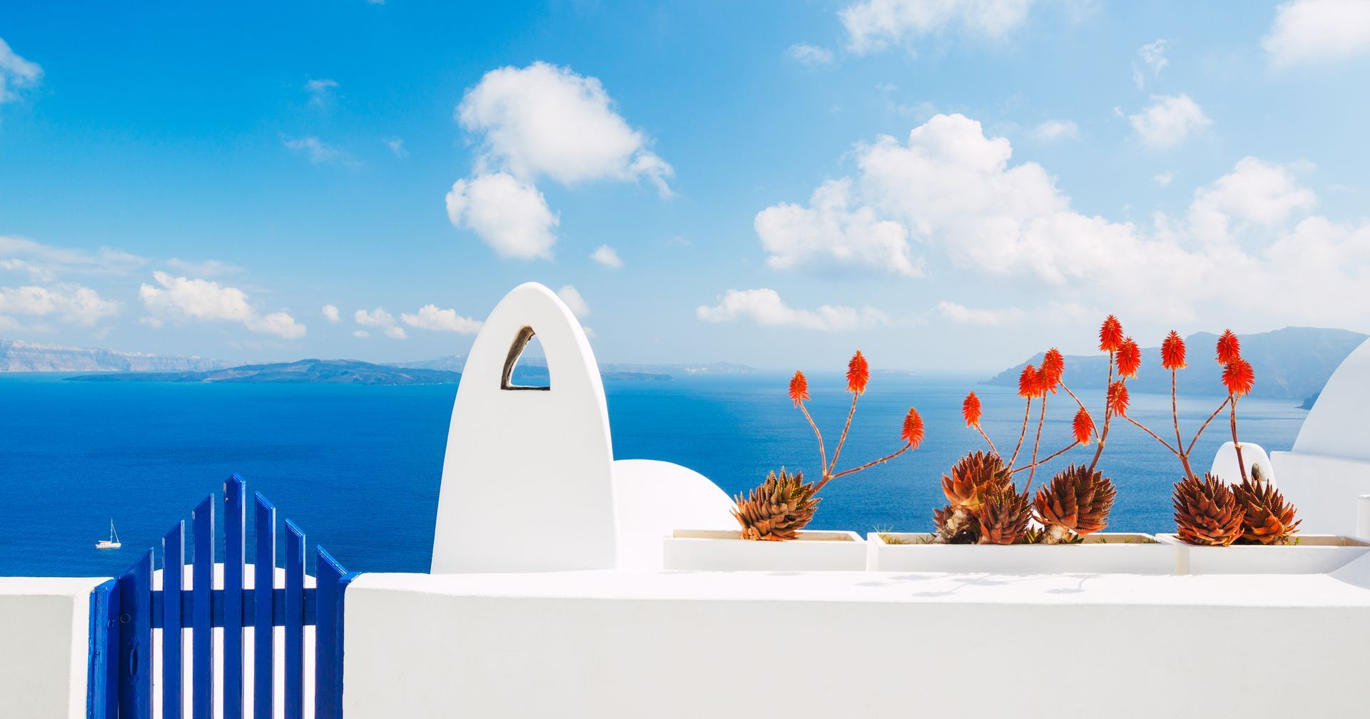 White building with blue accents overlooking the Aegean Sea under a blue sky with clouds.