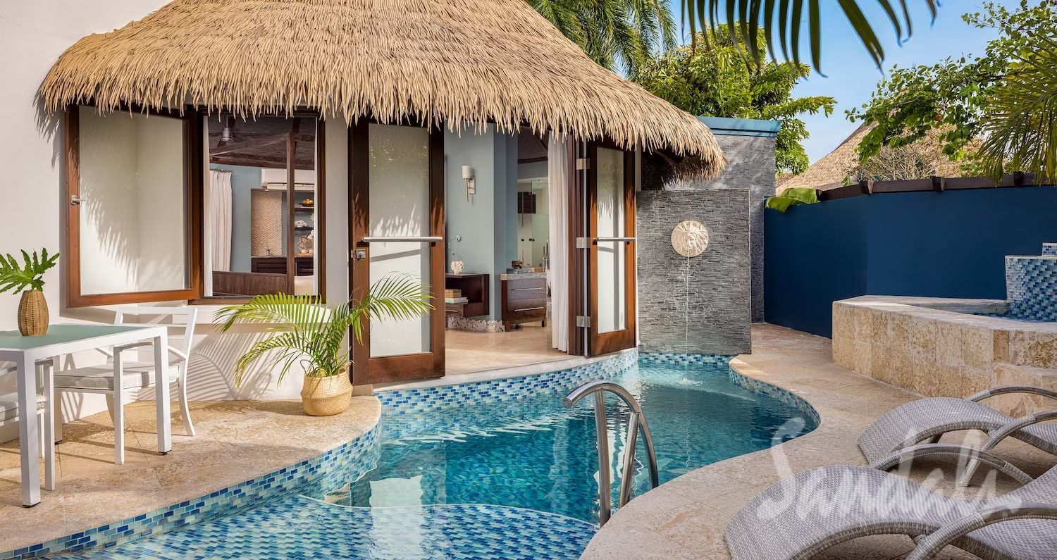 Tropical villa with a pool, straw roof, white walls, and outdoor seating.