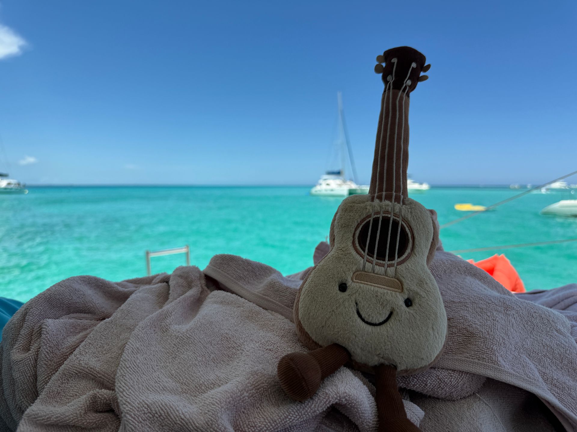 Kaia the Ukulele rests on a bench with turquoise seas behind her during a catamaran day trip to Isla